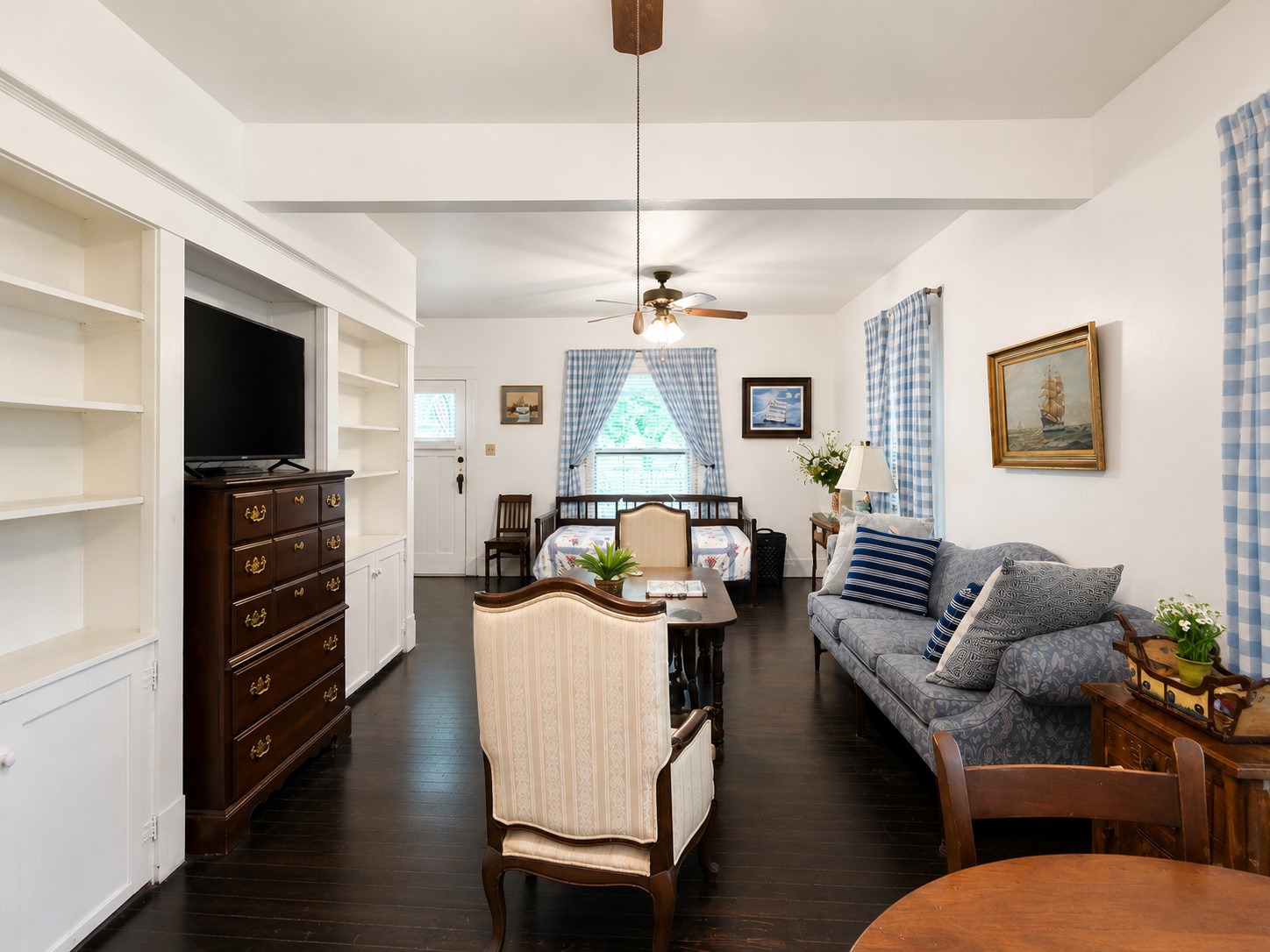 Wide-angle view showcases the spacious living area with built-in shelving and cabinetry, dark wood flooring, ceiling fans, and abundant natural light. The extended layout provides flexibility for multiple seating and gathering areas.