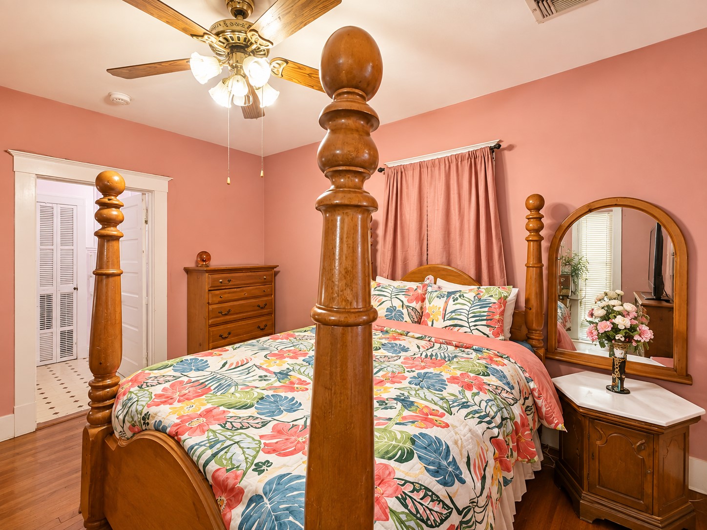 Spacious bedroom features warm wood flooring, classic white trim, a ceiling fan, and windows providing natural light. The room offers ample space for substantial bedroom furnishings.