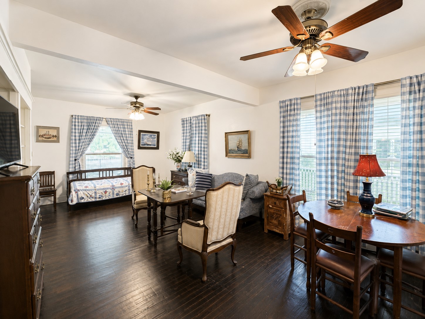 Expansive view highlights the flexible living and dining layout, accented by dark wood flooring and multiple windows that bring in abundant natural light. Two ceiling fans complement the spacious arrangement and help define the rooms distinct gathering areas.