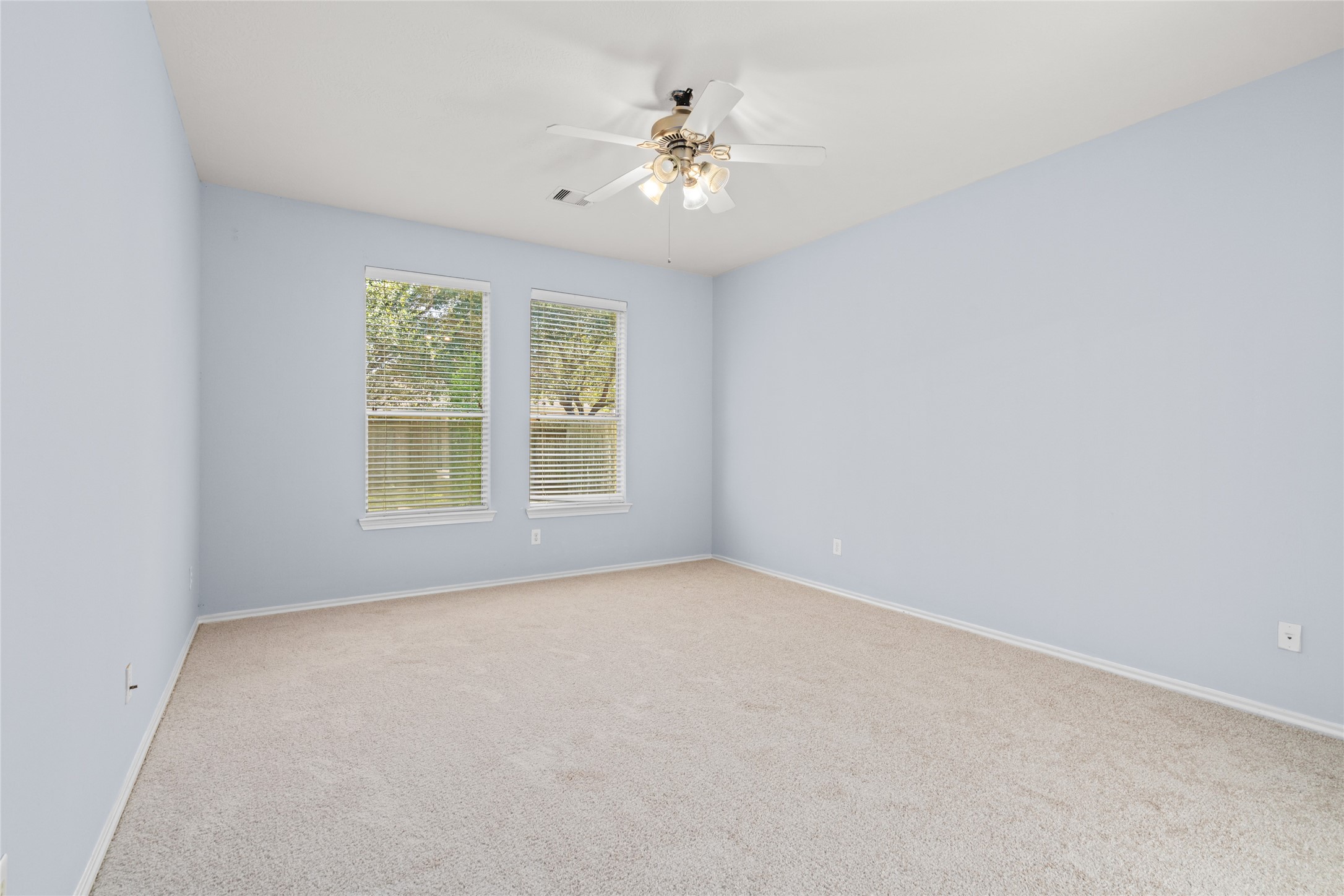 Unfurnished primary bedroom with soft carpeting, natural light from two windows, and a ceiling fan. The open floor area allows buyers to plan their preferred bedroom layout and personalize the space to suit their needs.