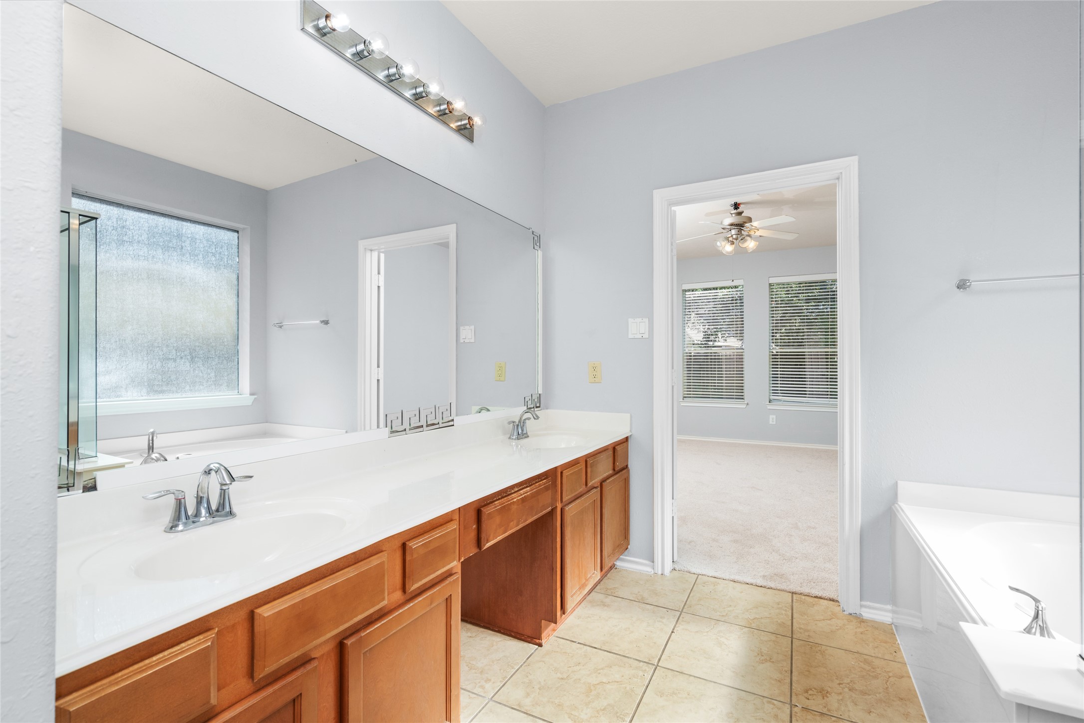 Spacious primary bathroom with a long double vanity, ample counter space, and a large window for natural light. The two-sink arrangement offers added convenience for shared morning and evening routines.