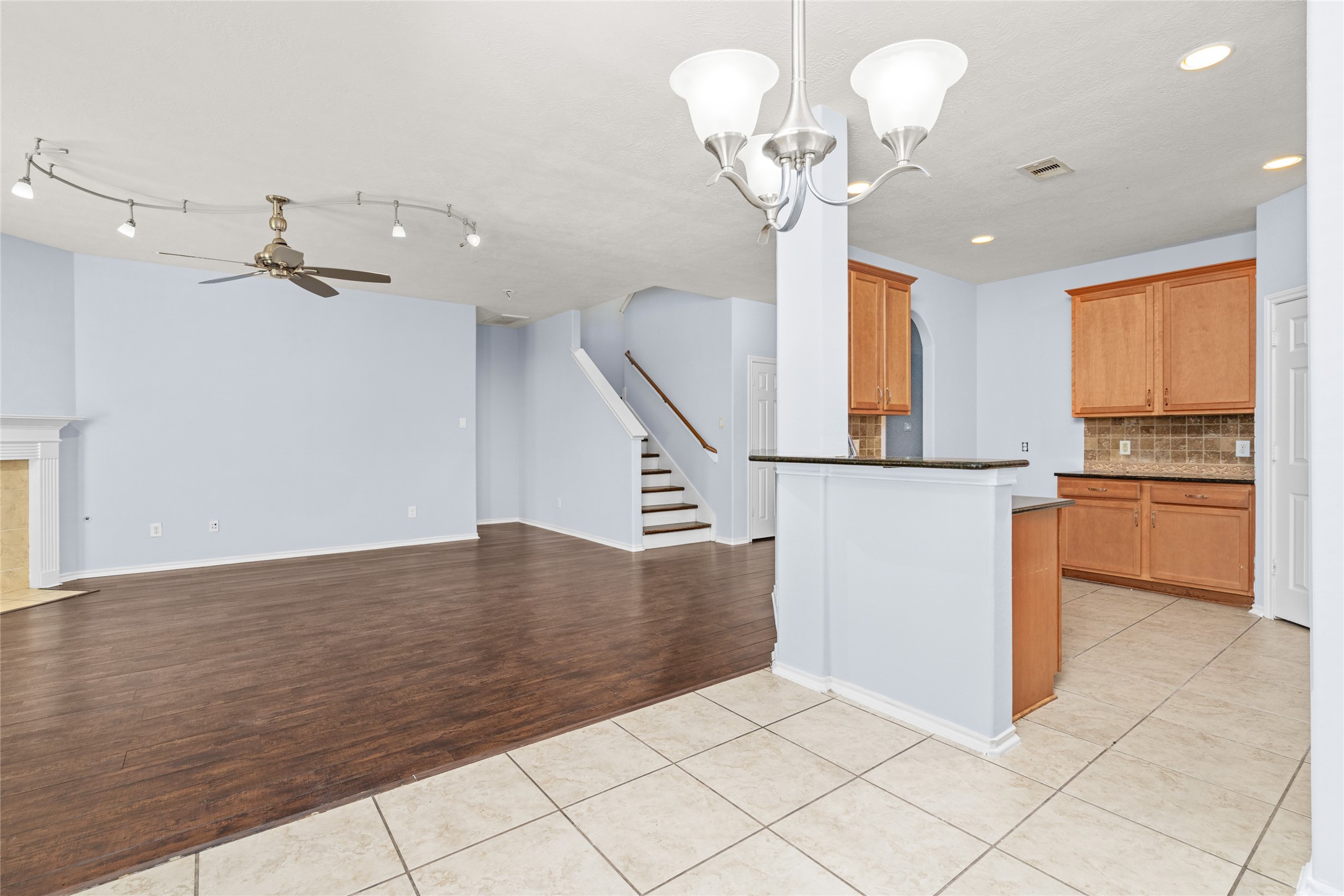 Open view connecting the kitchen, breakfast area, and living room, with the staircase visible beyond. The connected layout gives the main floor a spacious feel and allows activities in different areas to remain visually connected.