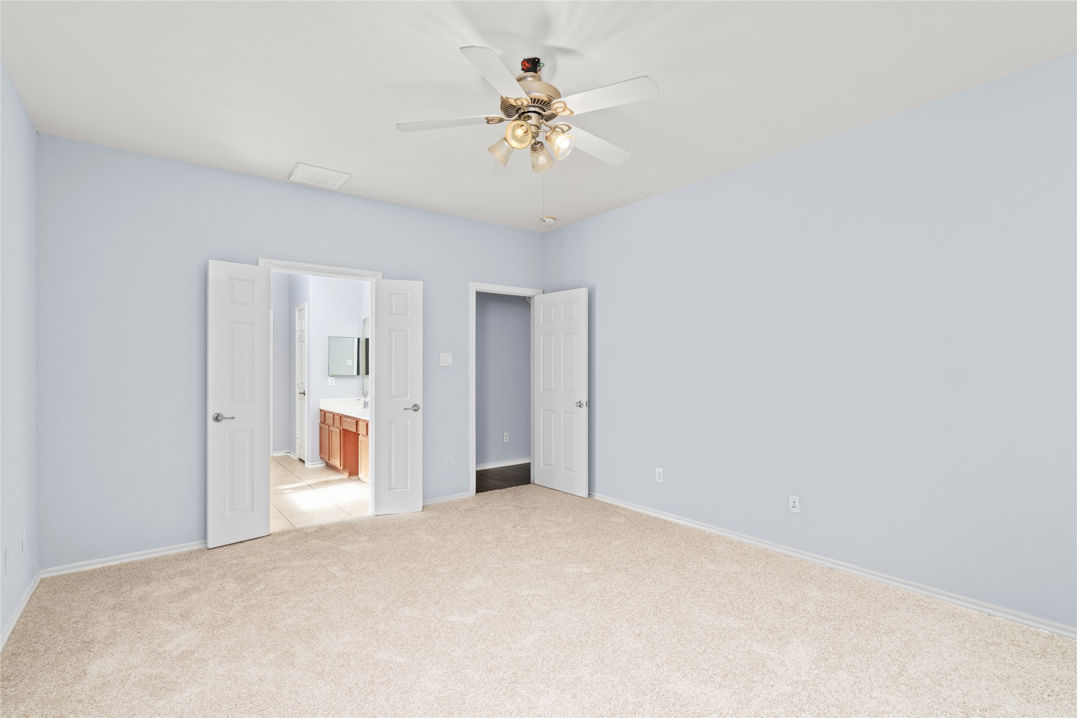 Alternate view of the primary bedroom highlighting its broad floor area, neutral wall color, soft carpeting, and doorway connections. The uncluttered layout offers flexibility for bedroom furniture and everyday movement.