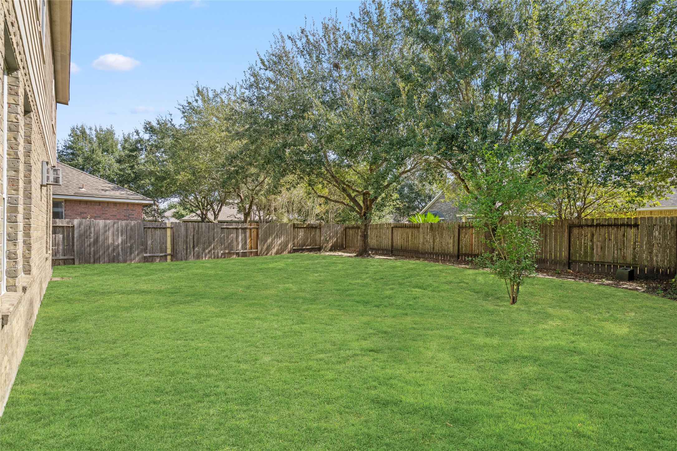 Spacious fenced backyard with a mature tree and open lawn extending across the rear of the property. The generous open area provides flexibility for outdoor recreation, gardening, or creating a personalized backyard retreat.