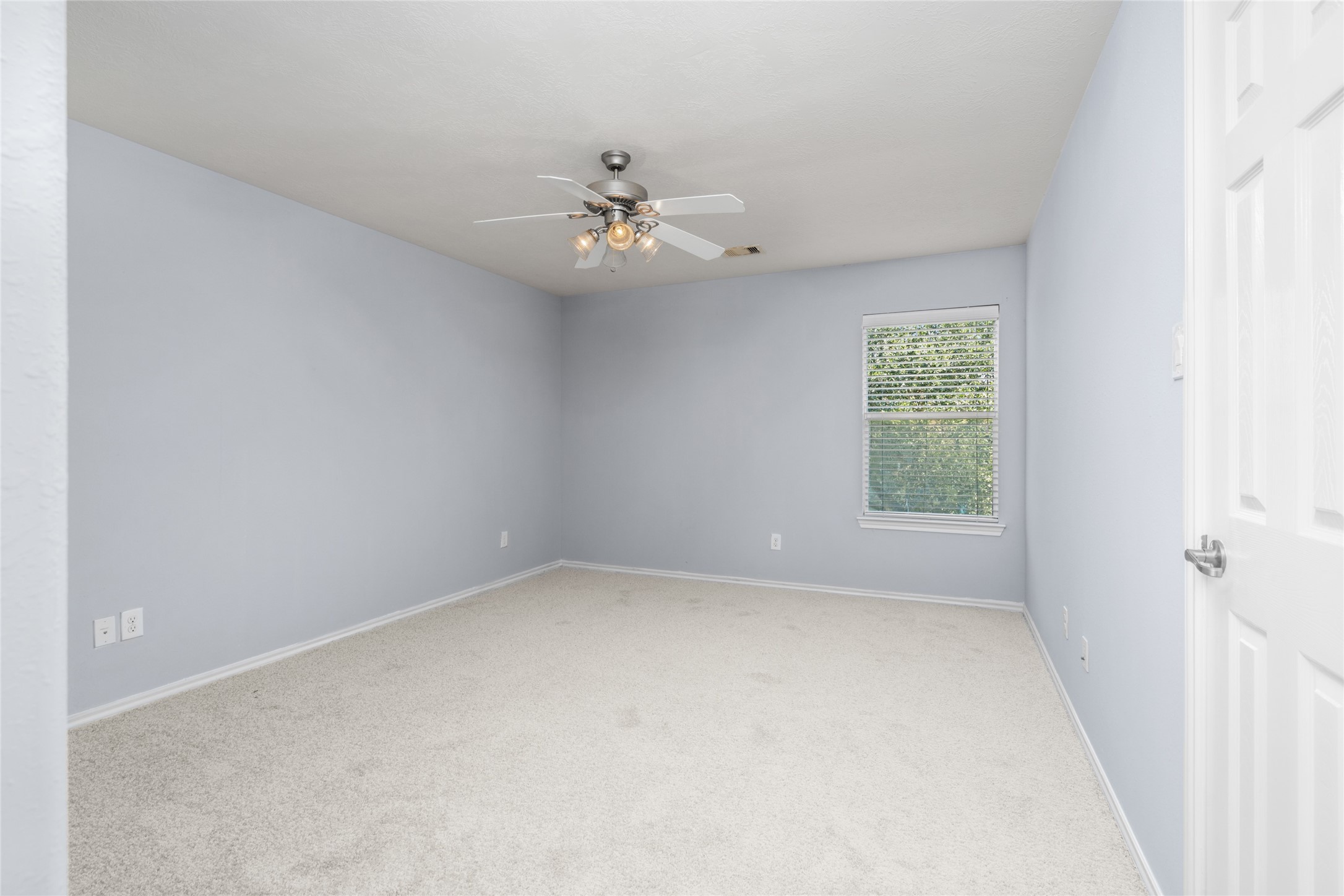 Additional bedroom view featuring soft carpeting, light blue walls, a ceiling fan, and natural light from the window. The straightforward layout offers a versatile space that can be adapted to different furniture arrangements and personal preferences.