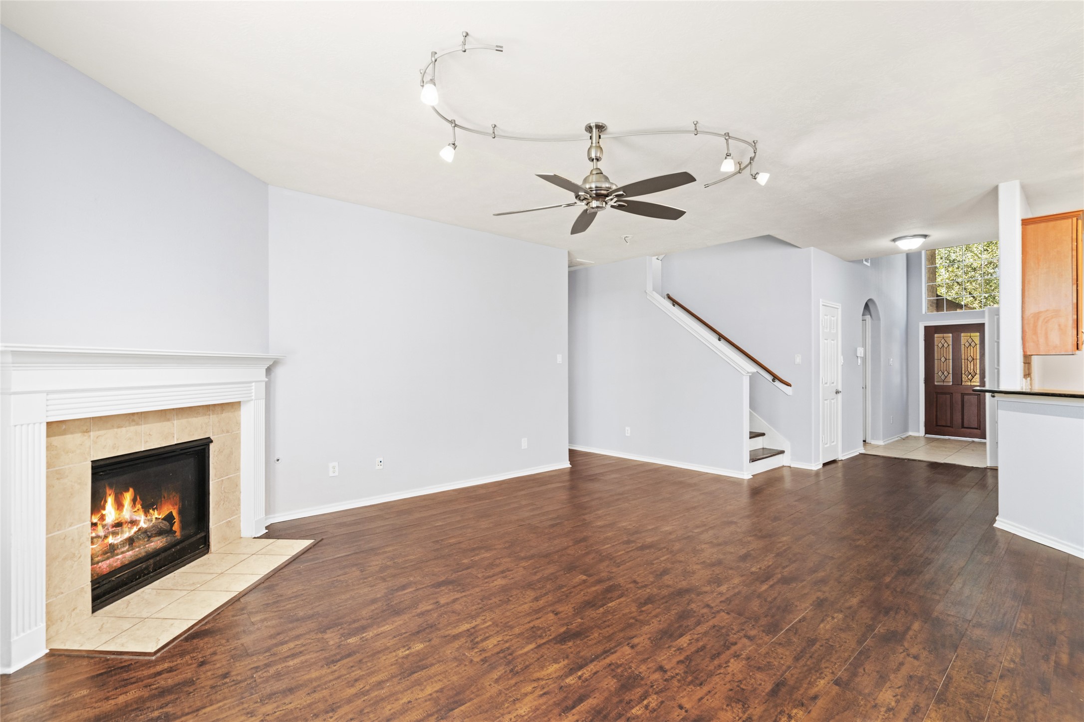 Spacious living room featuring wood flooring, a corner fireplace, and an open staircase. The generous floor area creates room for everyday relaxation and entertaining, while the fireplace provides a natural focal point.