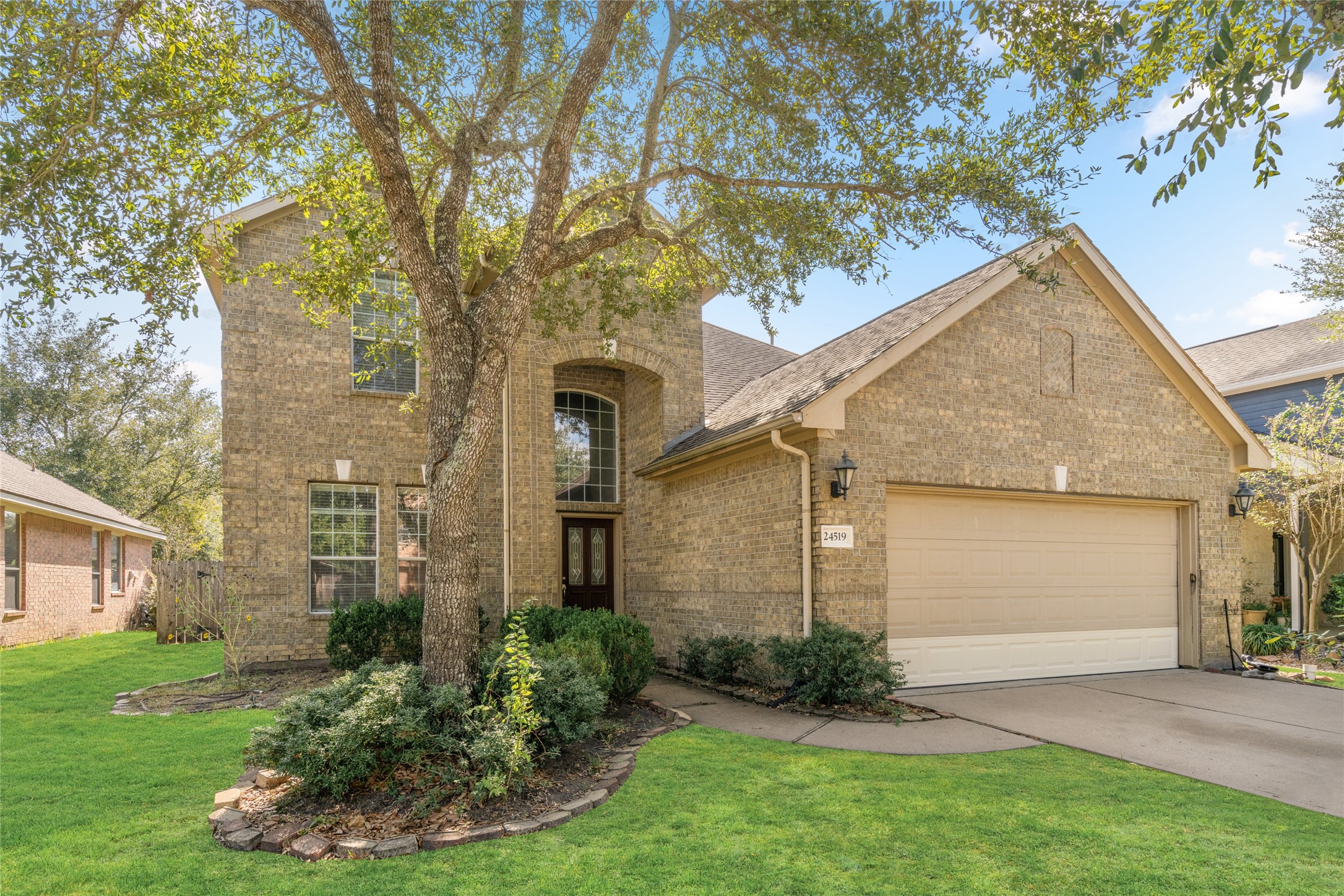 Full front view of the two-story brick home, highlighting its arched entryway, mature trees, and landscaped grounds. The combination of traditional brickwork and established greenery gives the property timeless neighborhood appeal.