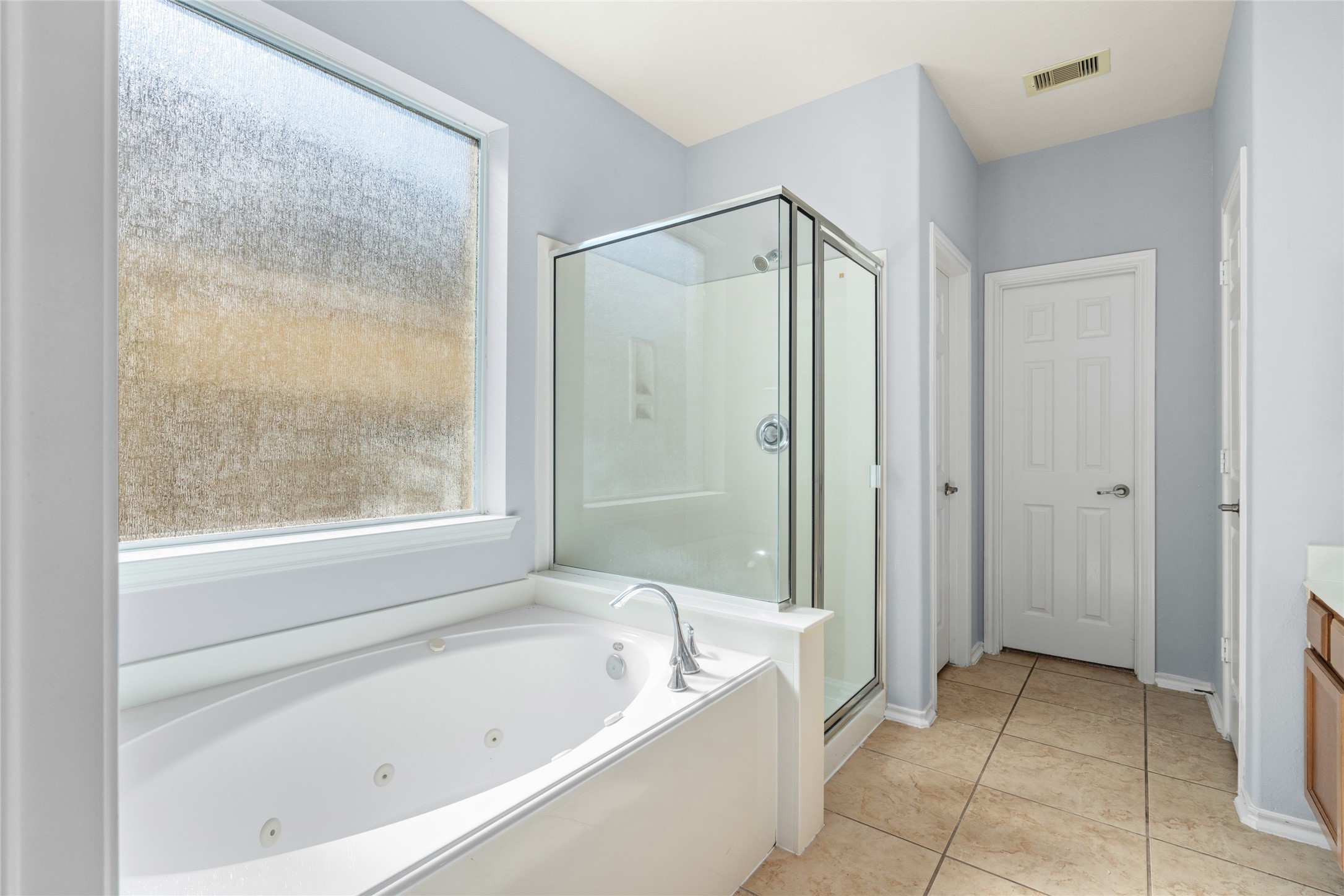 Primary bathroom featuring a corner jetted tub, separate glass-enclosed shower, and natural light from a large window. The separate bathing options provide flexibility for a quick morning routine or a more relaxing end-of-day soak.