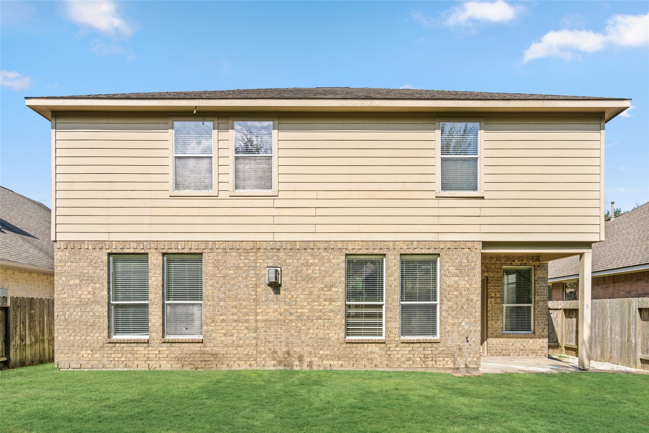 Full rear elevation showcasing the home's two-story design, multiple windows, and access to the backyard. The broad exterior view helps buyers understand the home's layout and how the indoor living spaces relate to the outdoor area.