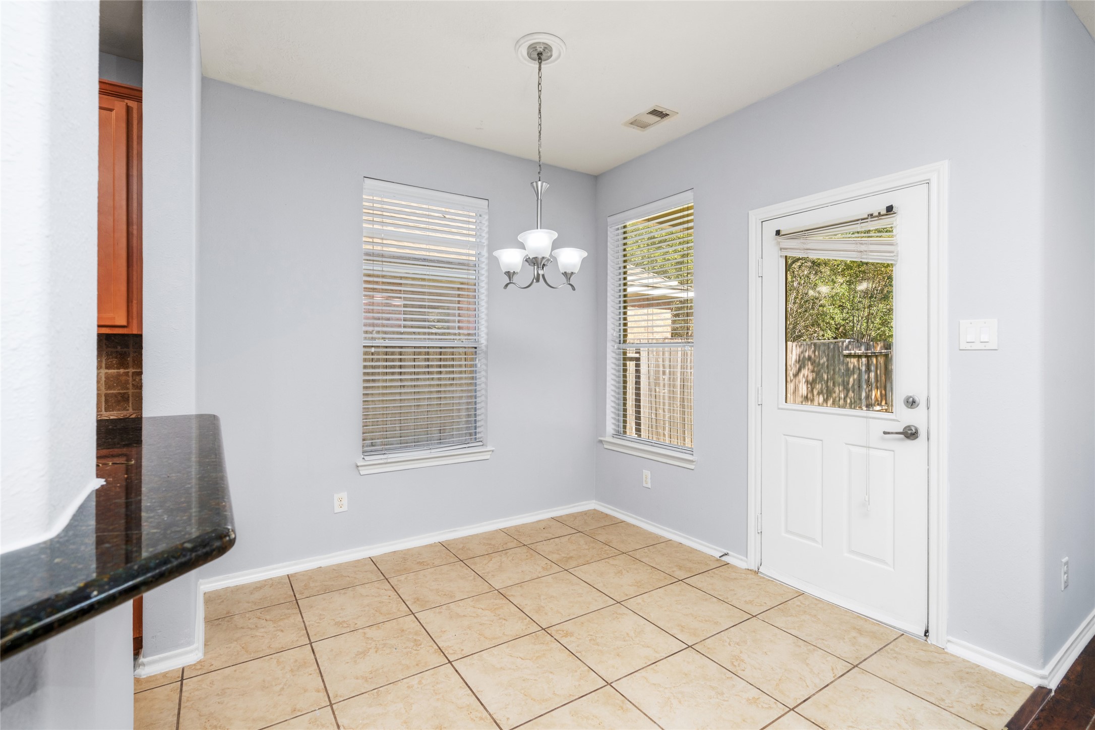 Bright breakfast area with tiled flooring, windows, and an exterior door overlooking the outdoor space. Its placement beside the kitchen makes daily dining convenient and provides a natural connection to the backyard.