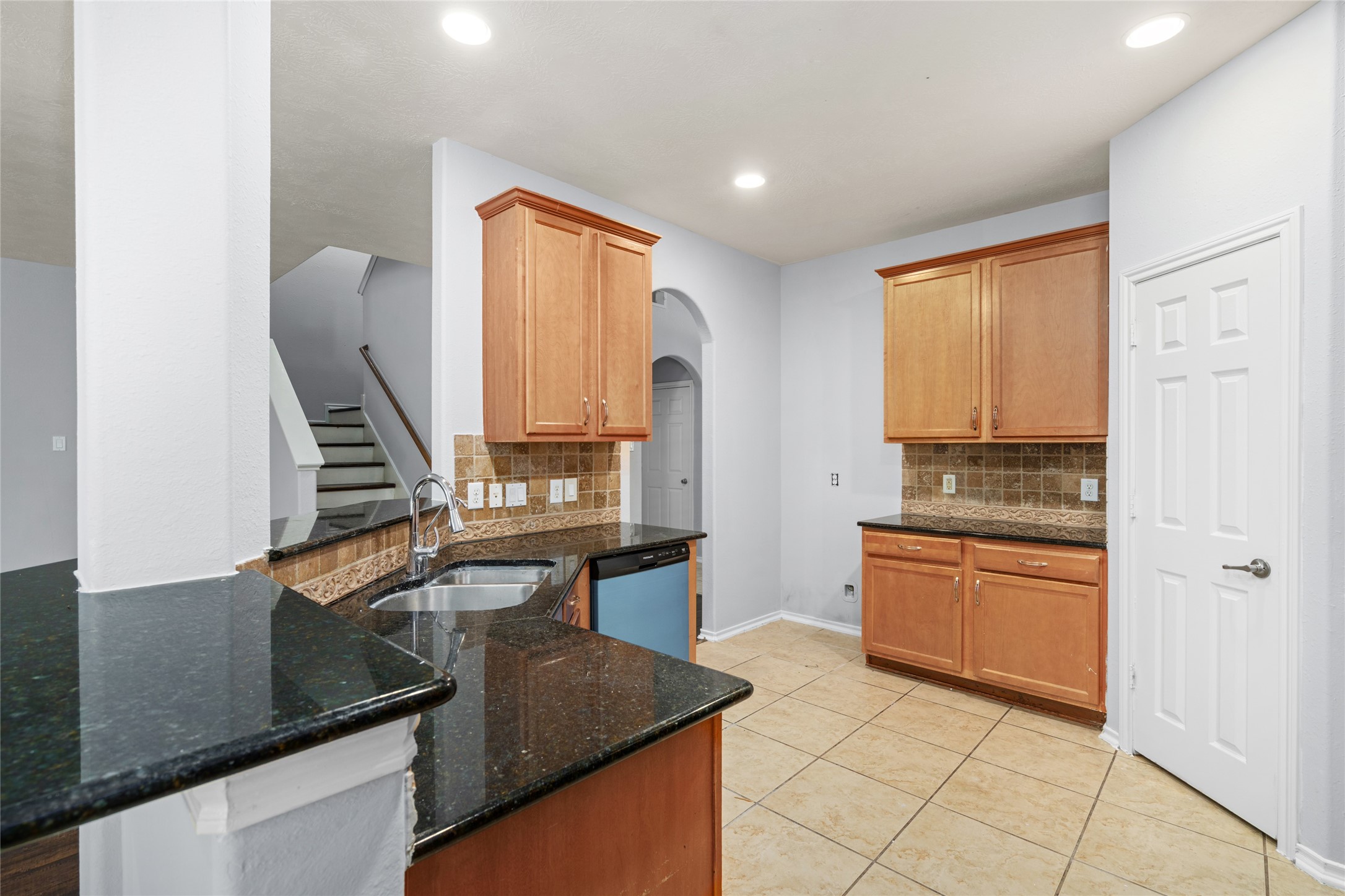 Kitchen featuring warm wood cabinetry, black granite countertops, and a breakfast bar overlooking the adjoining living space. The counter area provides additional workspace for meal preparation and a convenient place for casual dining.