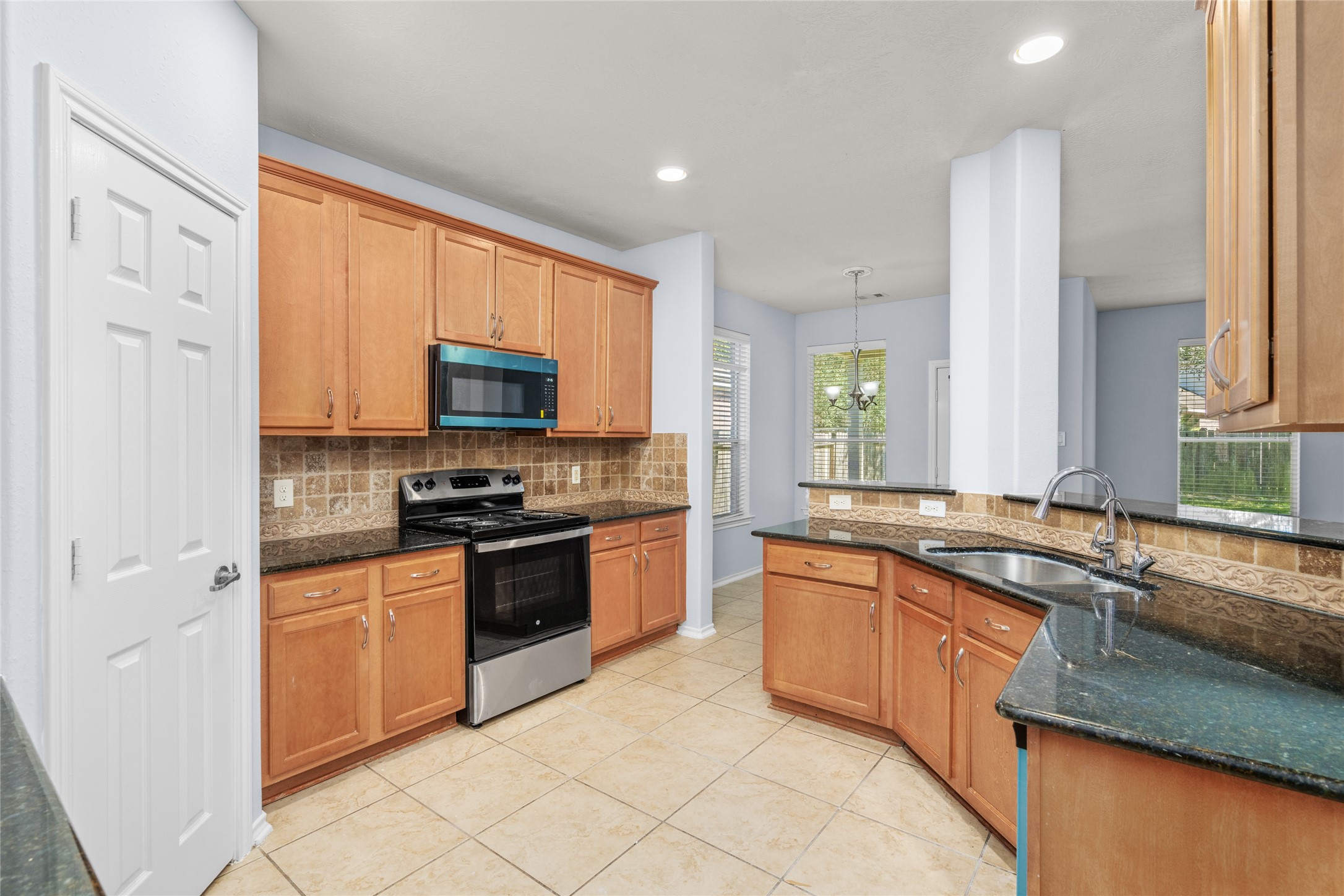 Alternate kitchen view highlighting the cabinetry, black granite work surfaces, built-in microwave, electric range, and tiled flooring. The combination of storage and accessible counter space supports an efficient everyday cooking routine.