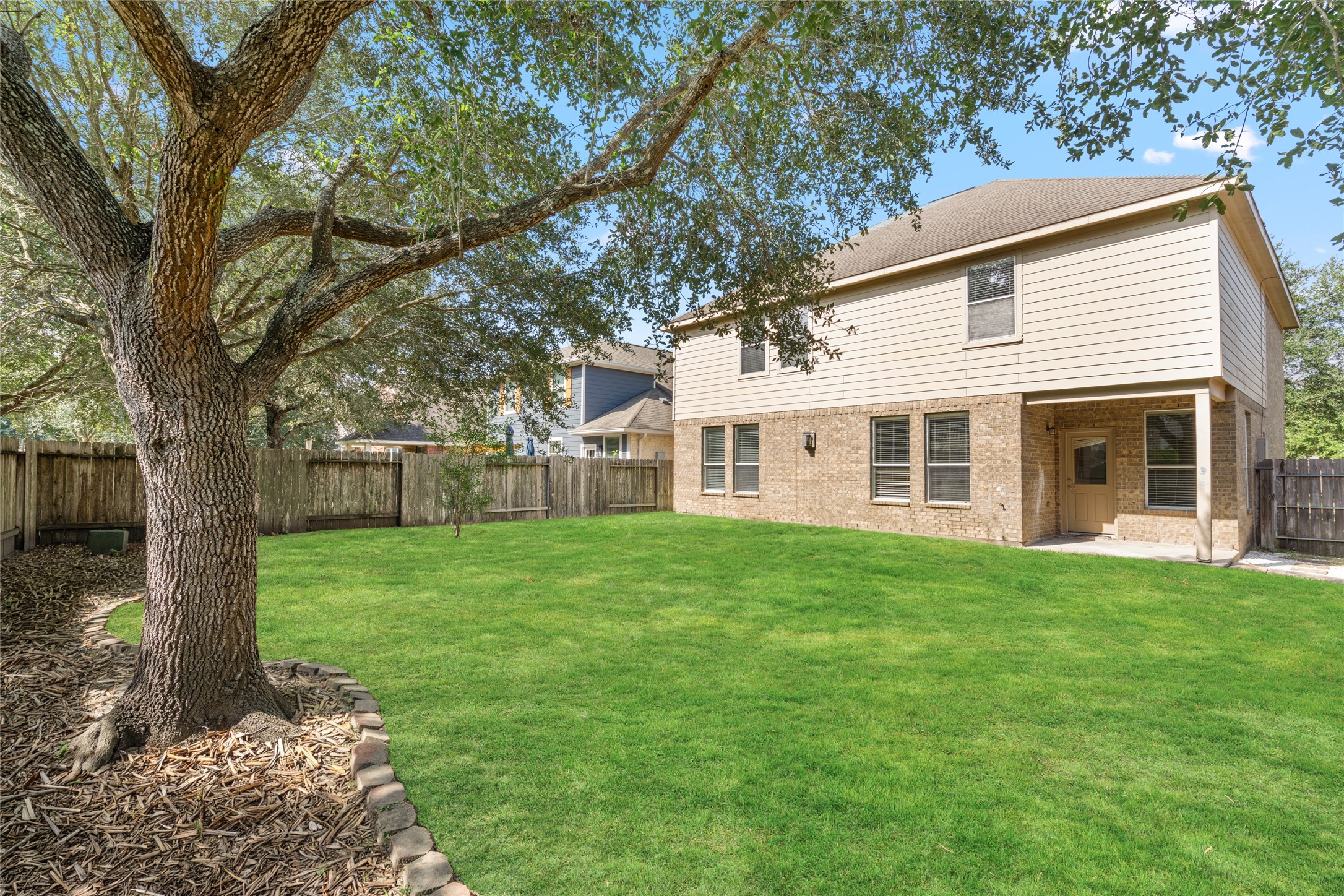 Broad backyard view showcasing the green lawn, mature shade tree, and wood privacy fencing. The open outdoor space offers room for play, gardening, outdoor seating, or other activities suited to the household. Broad backyard view showcasing the green lawn, mature shade tree, and wood privacy fencing. The open outdoor space offers room for play, gardening, outdoor seating, or other activities suited to the household.