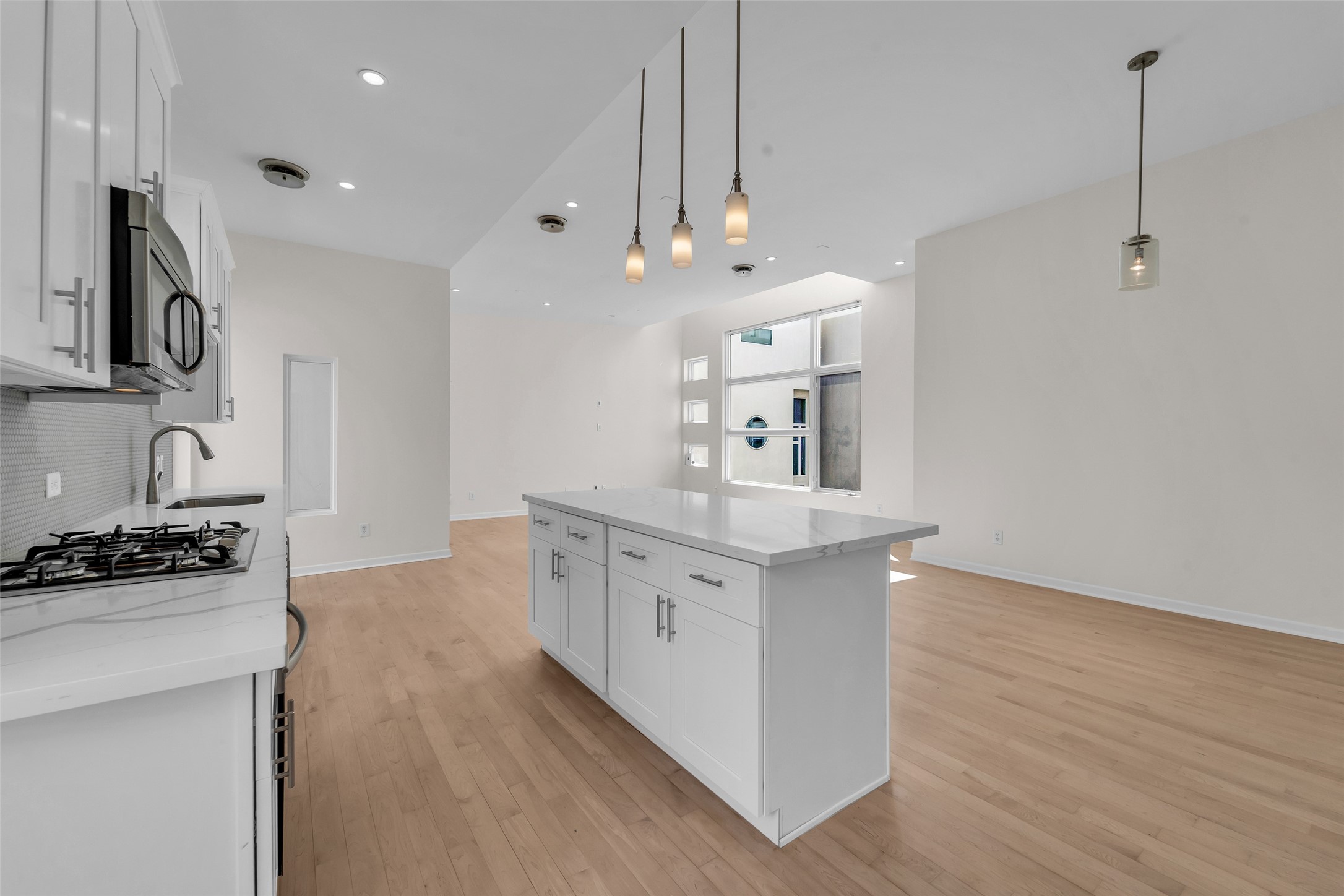 Modern kitchen with sleek white cabinetry, a spacious island, and elegant pendant lighting, seamlessly flowing into an open living area with abundant natural light.