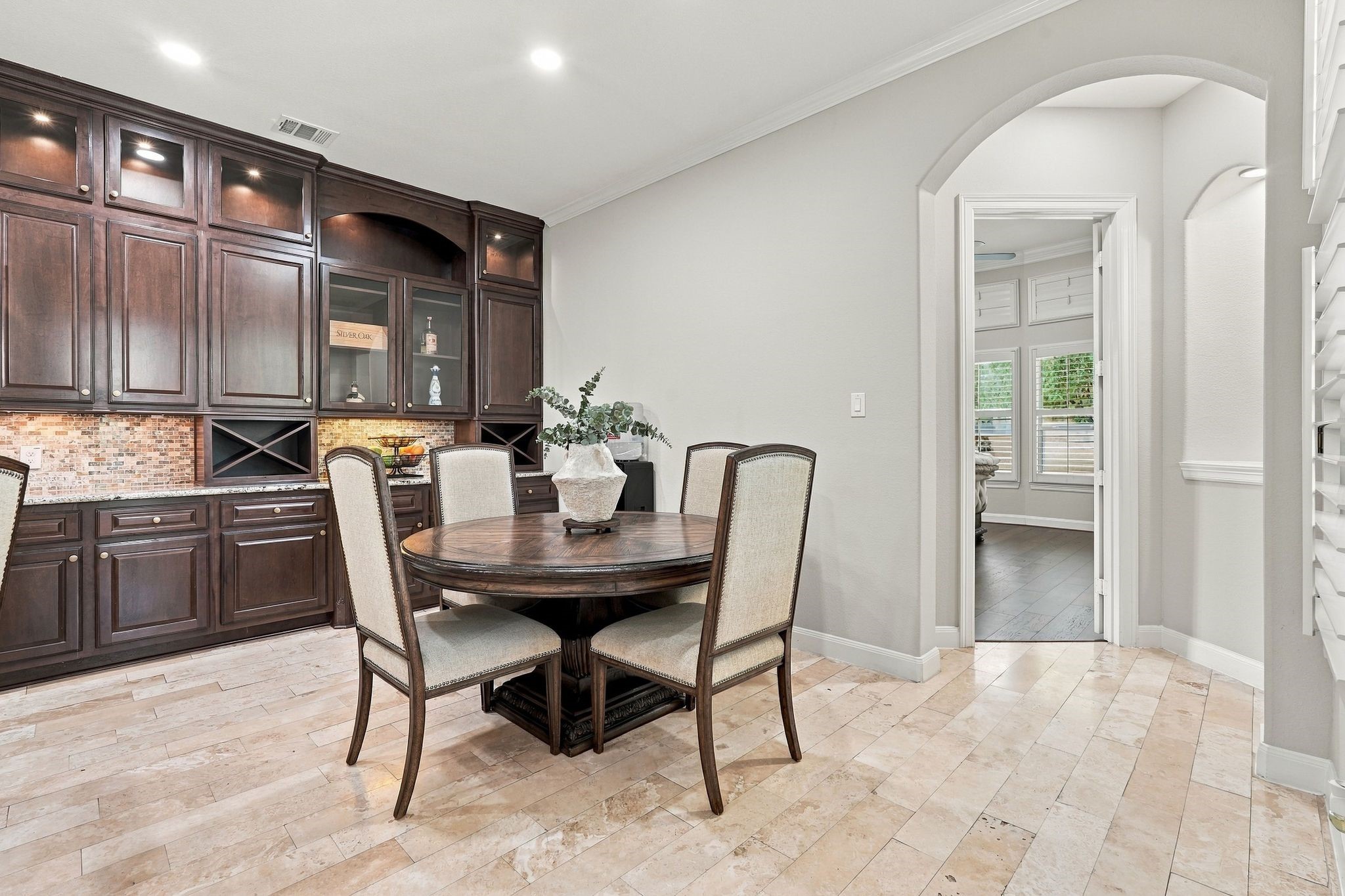 Beautifully appointed breakfast area featuring elegant travertine flooring and custom cabinetry with glass-front display cabinets, built-in wine storage, granite countertops, and under-cabinet lighting. The dedicated coffee and wine bar adds both luxury and functionality, creating the perfect space for casual dining and effortless entertaining.