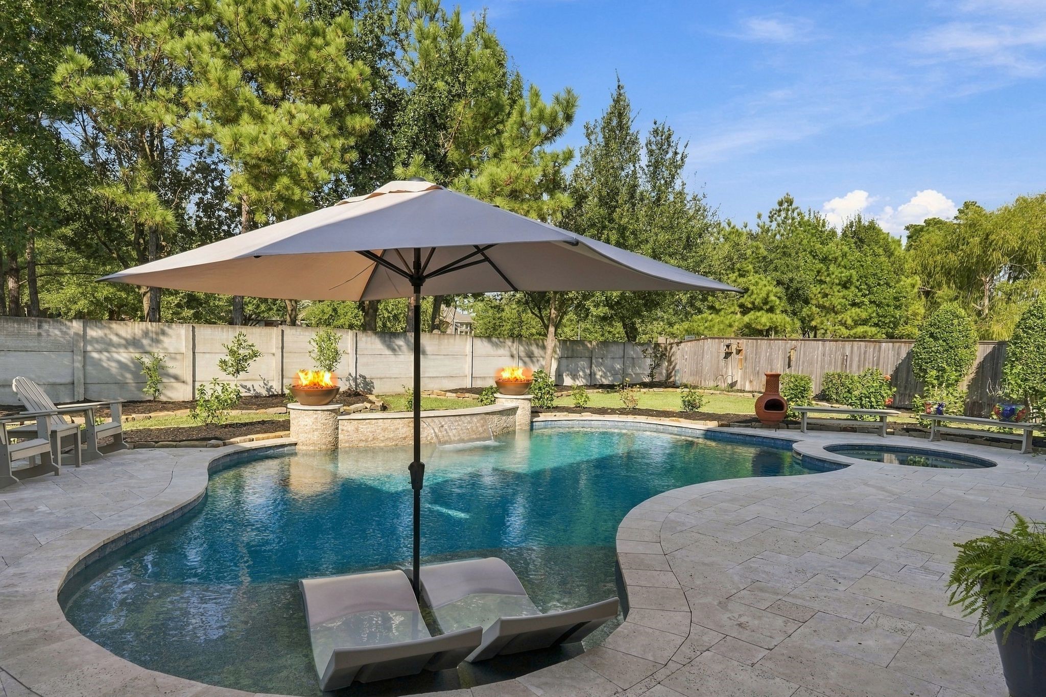 Spectacular backyard oasis featuring a custom-designed resort-style pool with tanning ledge, in-water loungers, dramatic fire bowls, cascading water features, and an adjoining spa. Expansive decking and lush landscaping create an exceptional setting for outdoor entertaining and relaxation.