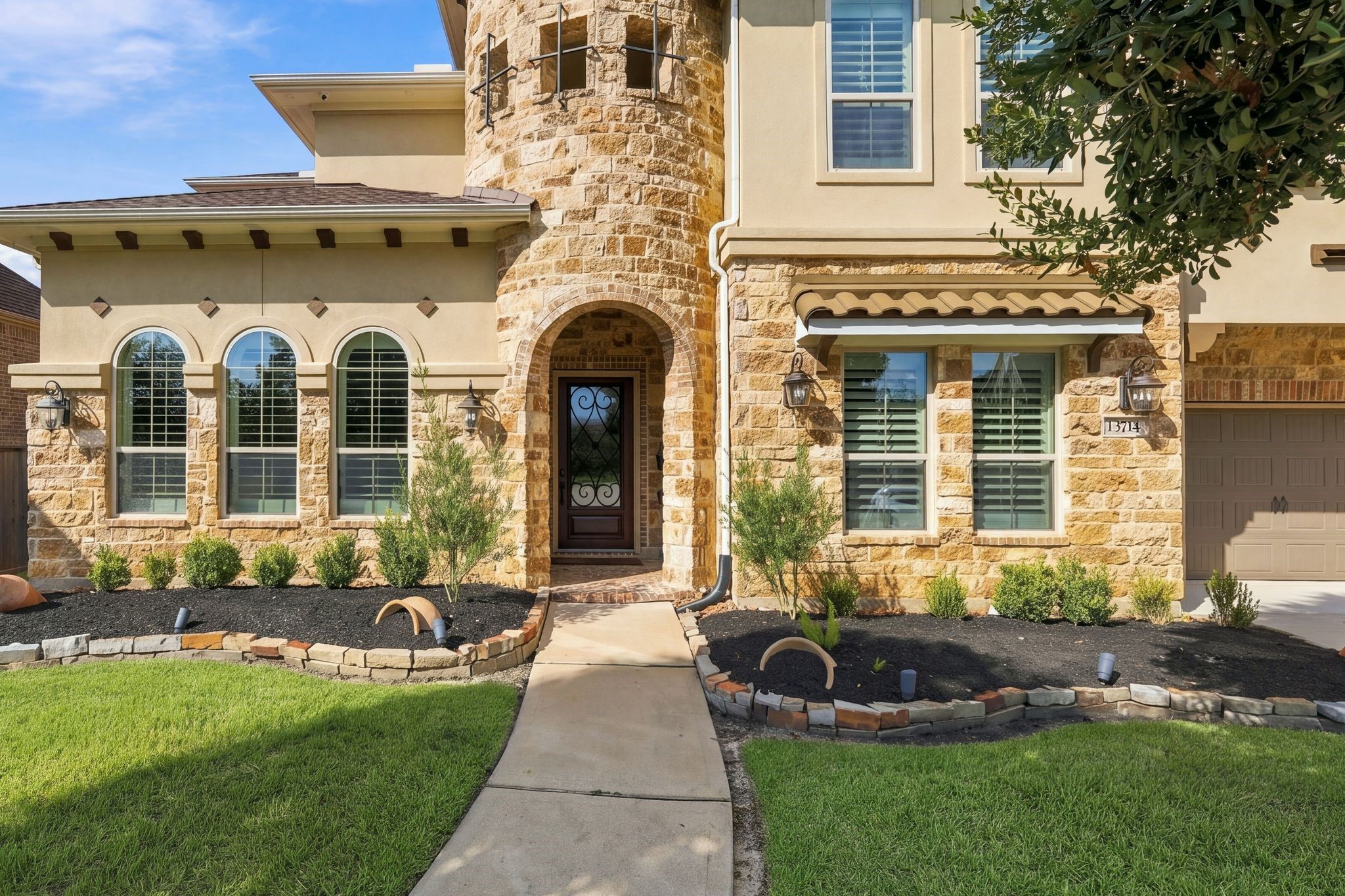 Impressive front entry featuring a distinctive natural stone turret, beautiful arched windows, decorative wrought-iron glass front door, and elegant architectural details. Professionally maintained landscaping enhances the exceptional curb appeal of this luxury home in gated Wildwood at Northpointe.