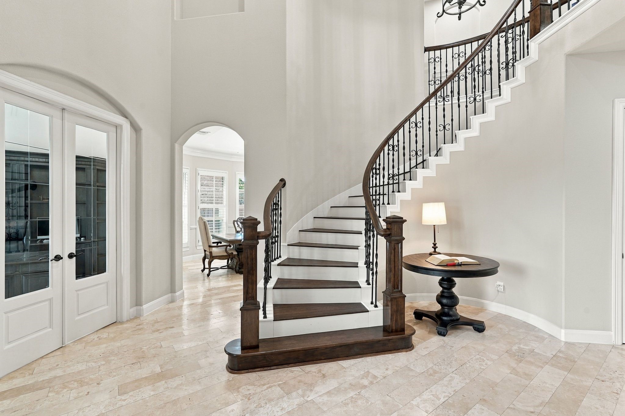 Grand two-story foyer featuring a stunning curved staircase with rich wood treads, decorative wrought-iron balusters, elegant travertine flooring, and soaring ceilings. Beautiful architectural details create an impressive first impression upon entering this luxury home.