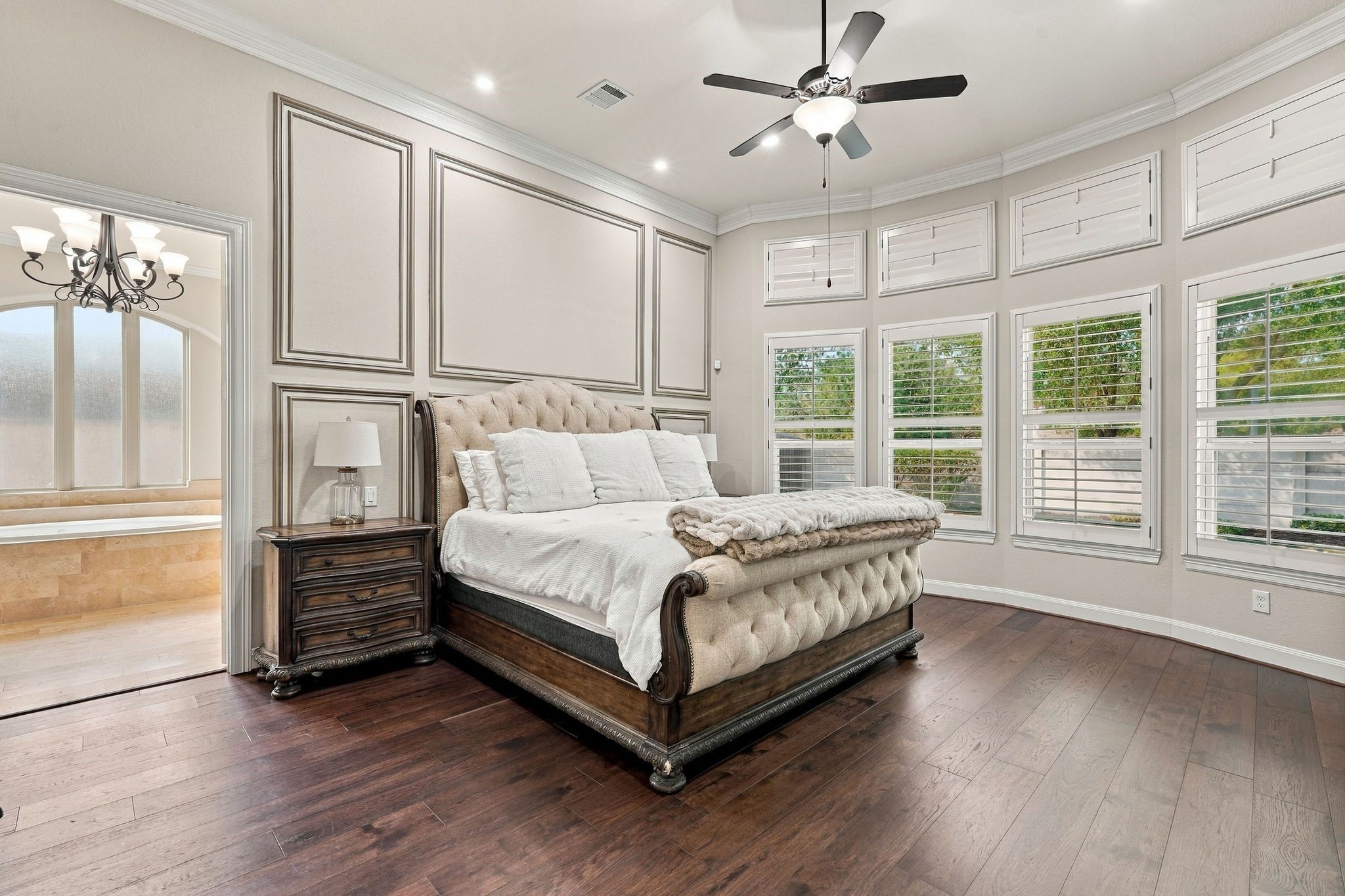 Luxurious primary suite offers a serene retreat with beautiful hardwood flooring, elegant custom wall molding, and a wall of windows adorned with plantation shutters. The spacious design, abundant natural light, and direct access to the spa-inspired ensuite bathroom create the perfect blend of sophistication and comfort.