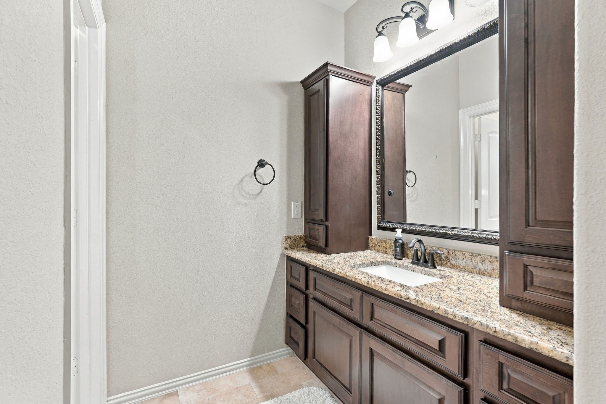 Jack-and-Jill bathroom features a private vanity area with granite countertops, rich wood cabinetry, generous storage, and elegant framed mirror. A thoughtfully designed layout provides convenient access and privacy for the adjoining bedrooms.