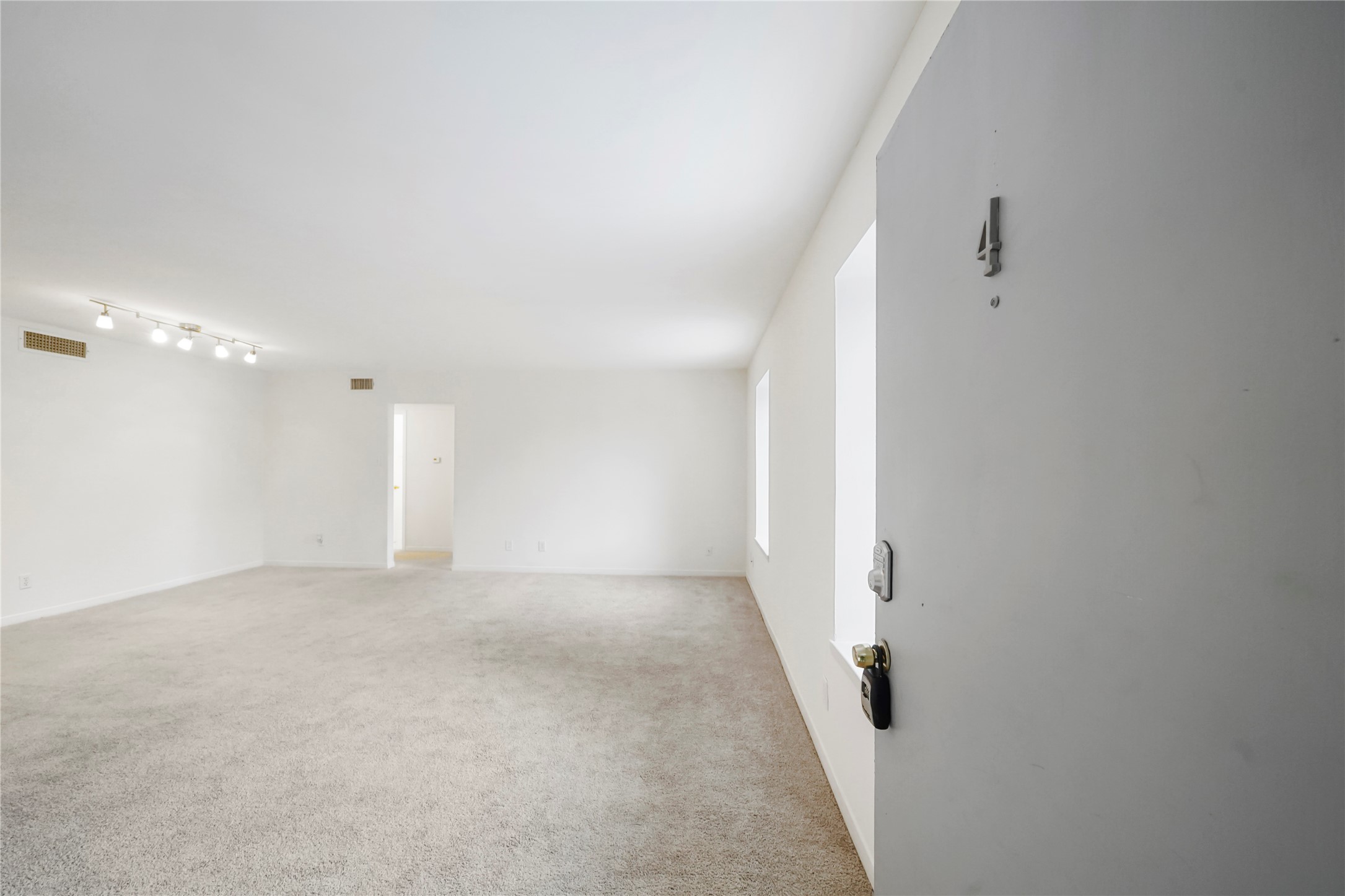 Welcome home view looking into the wide open living area directly from the front entrance, featuring fresh neutral paint, plush carpet, and overhead track lighting.