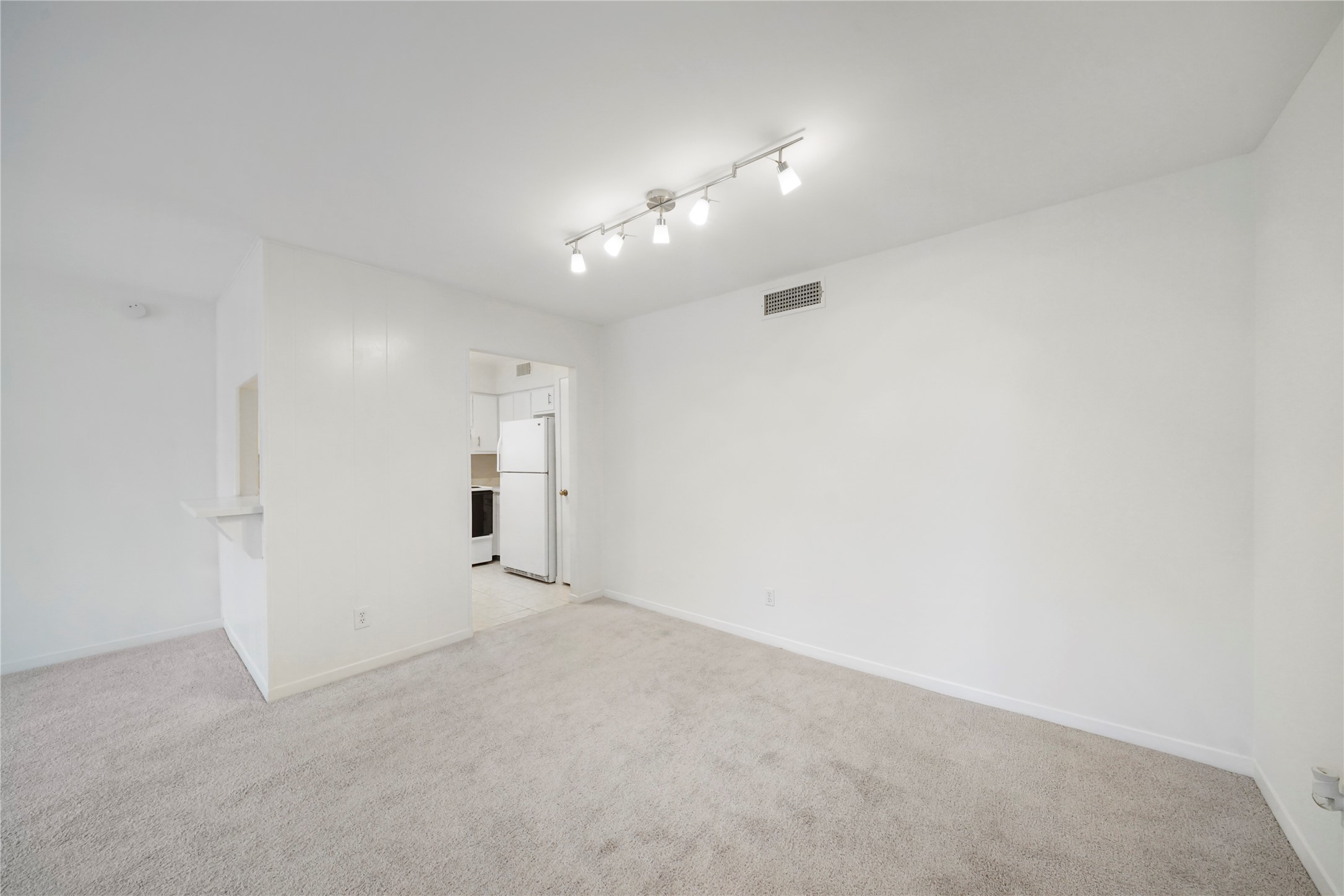 Dedicated dining or multi-purpose living area complete with neutral plush carpeting, modern overhead track lighting, and convenient pass-through counter access.