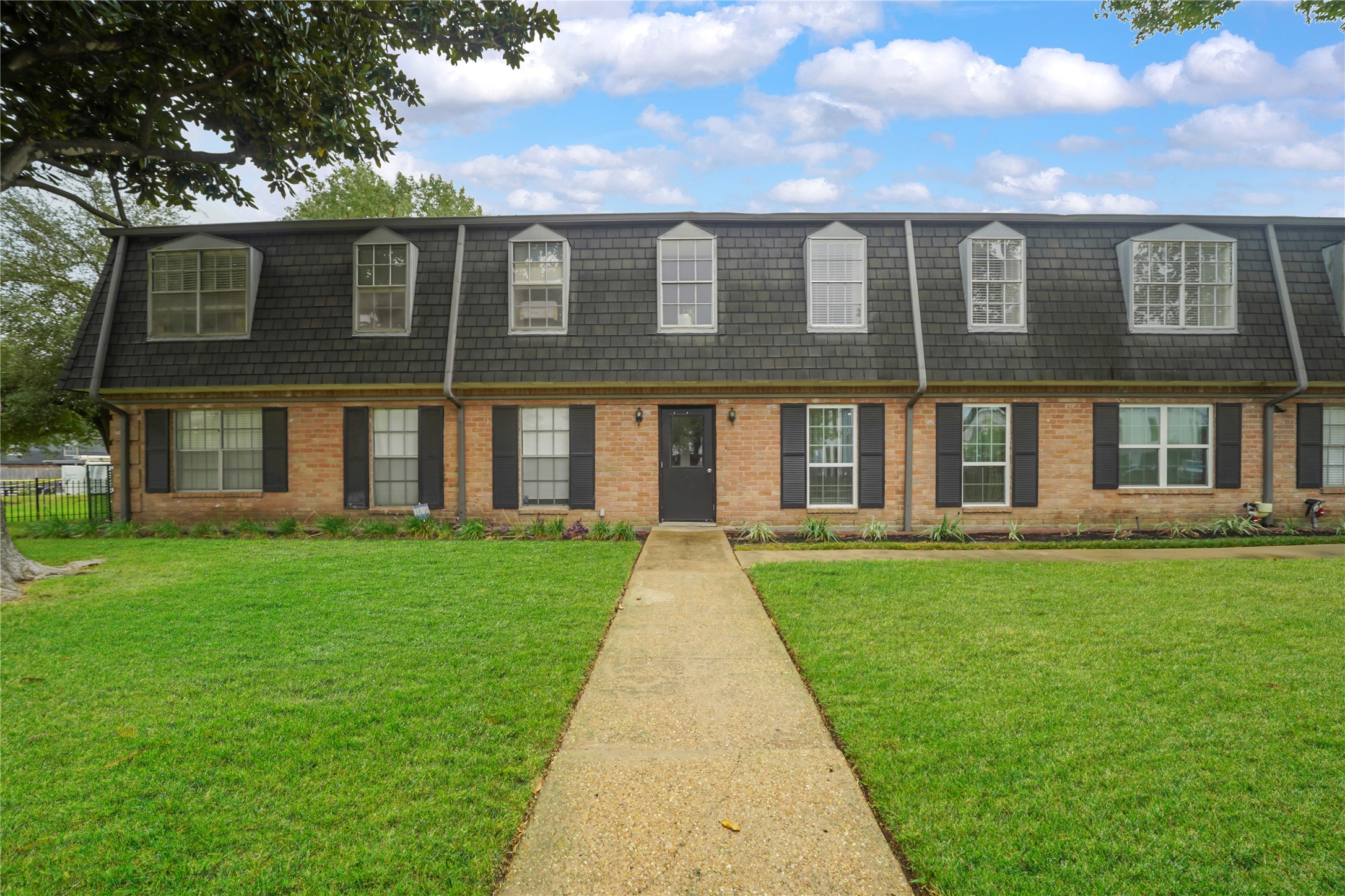 Front exterior elevation displaying a welcoming paved path leading to the private entry framed by manicured landscaping and mature trees.