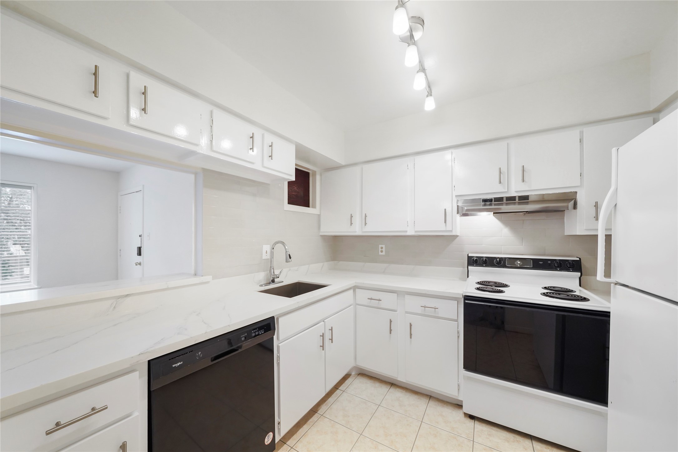 Kitchen highlight showcasing modern white cabinets, clean line counters, electric range, dishwasher, and pass-through counter to the dining room.