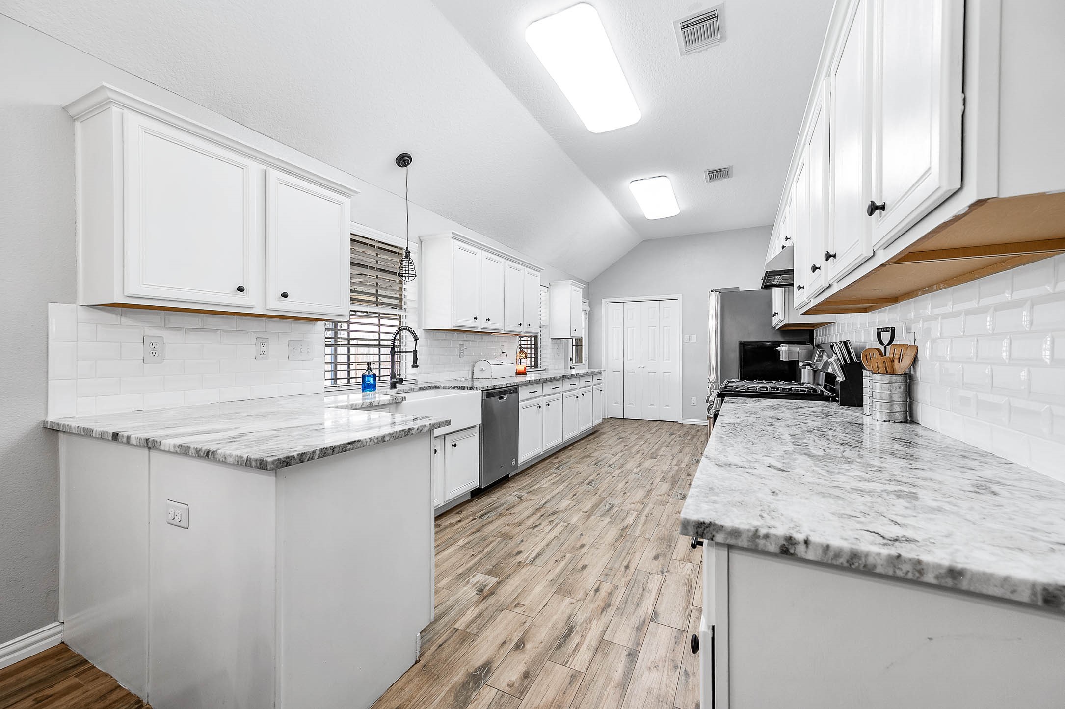 A spacious kitchen featuring elegant marble countertops, sleek stainless steel appliances, and bright white cabinetry, complemented by wood-look flooring and ample natural light.