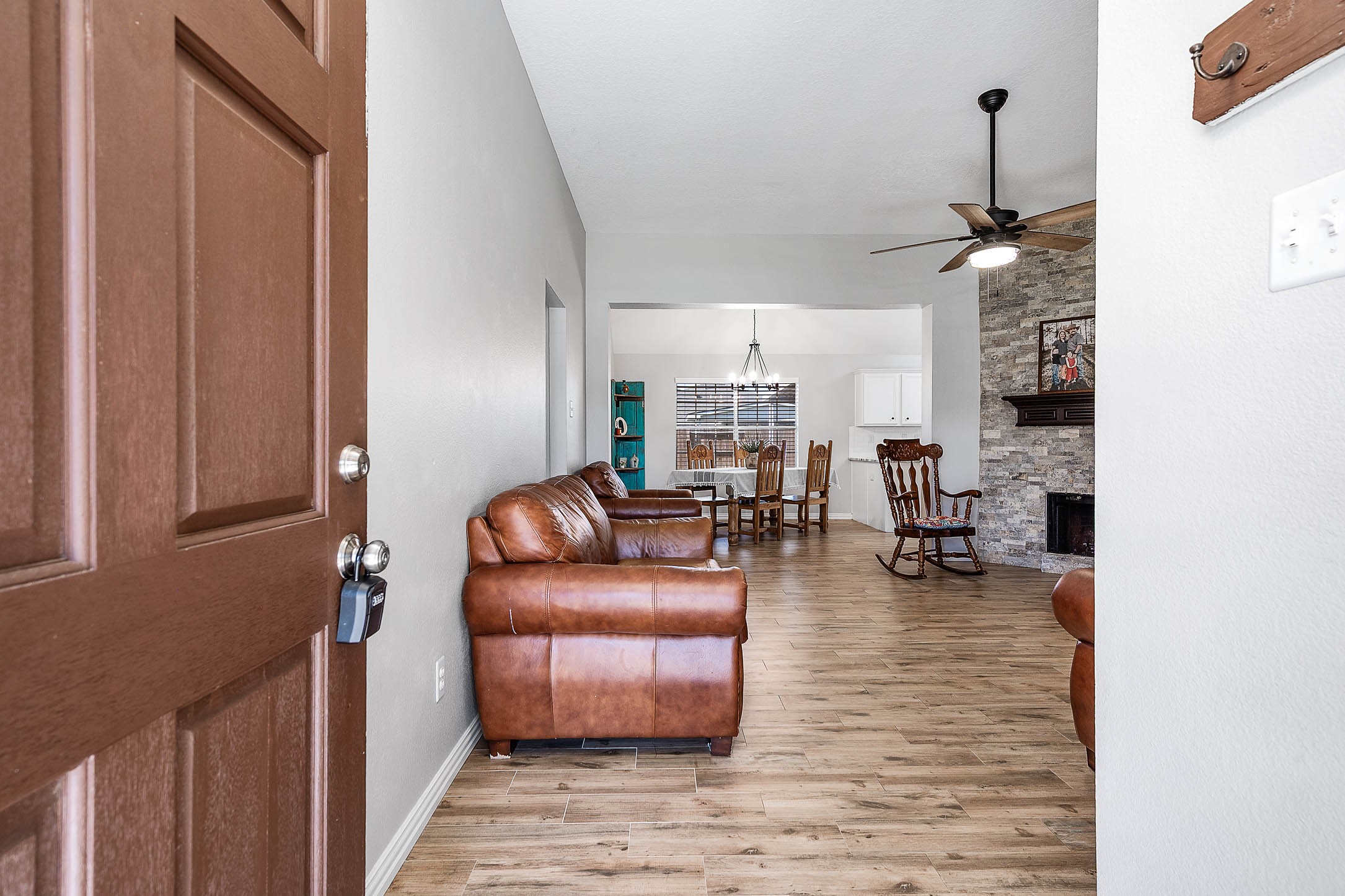 Step into a spacious open living area featuring warm wood floors, a cozy stone fireplace, and a ceiling fan, seamlessly connecting to a dining space with abundant natural light. Step into a spacious open living area featuring warm wood floors, a cozy stone fireplace, and a ceiling fan, seamlessly connecting to a dining space with abundant natural light.