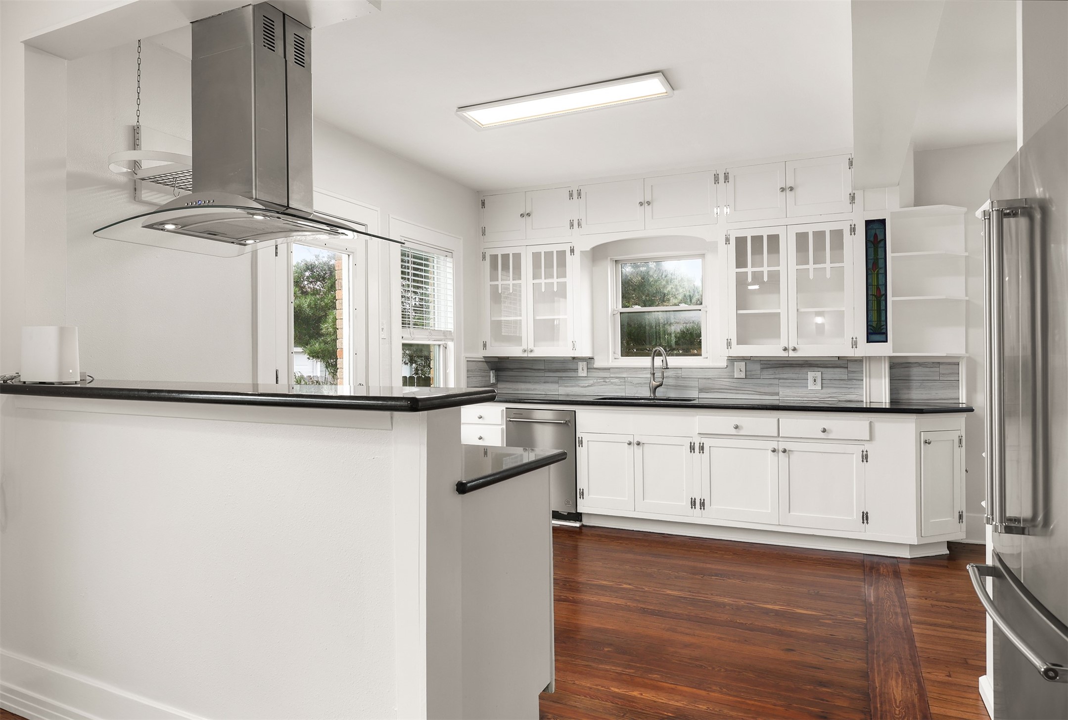Charming kitchen with white cabinetry, sleek dark countertops, and rich hardwood floors, featuring modern stainless steel appliances.