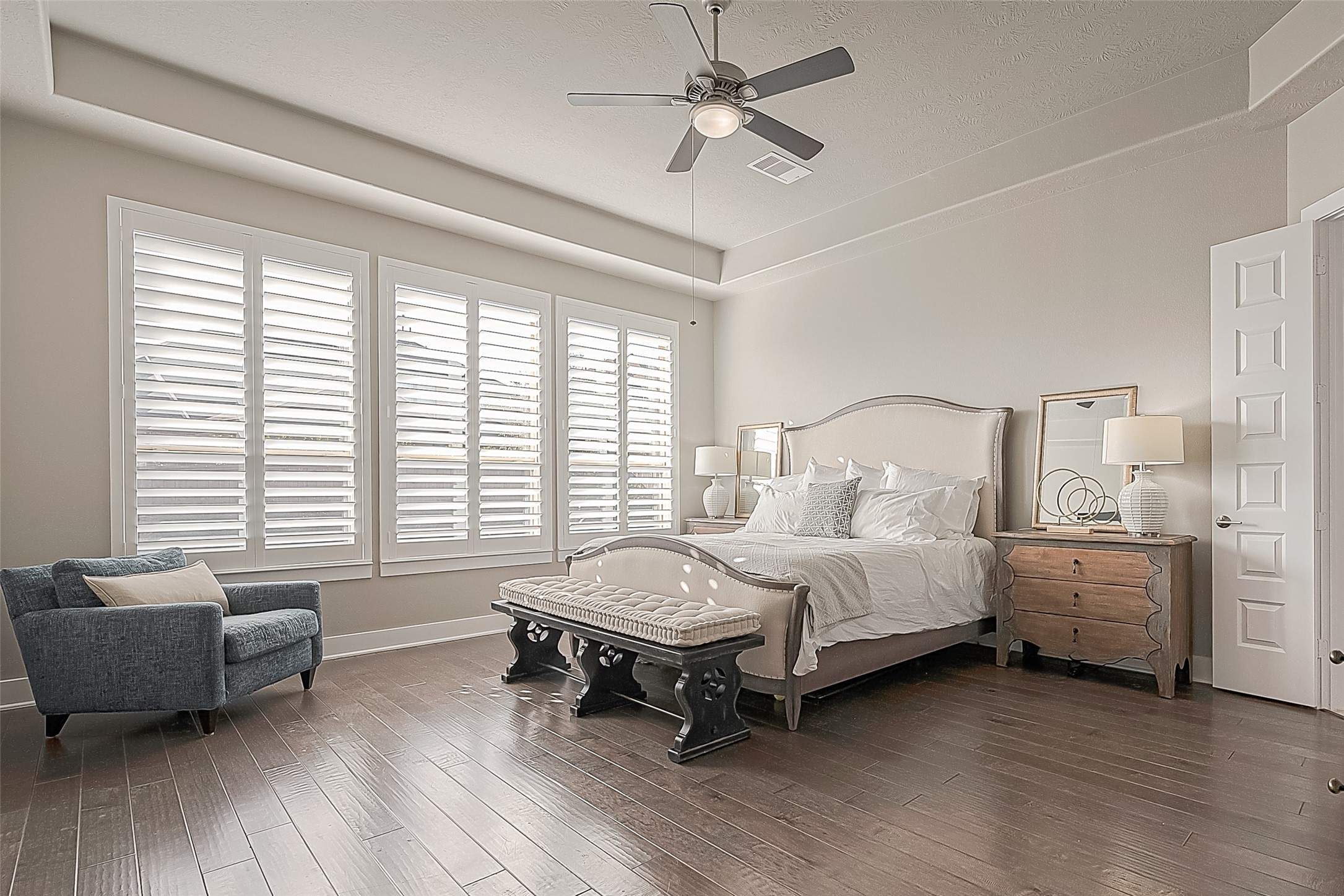 The expansive primary bedroom features inviting warm wood flooring, Plantation shutters, a ceiling fan, and ample space for a king bed and additional seating.
