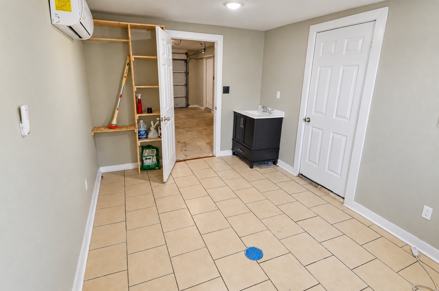 Spacious utility room featuring tiled floors, a compact sink, storage shelves, and access to the garage.