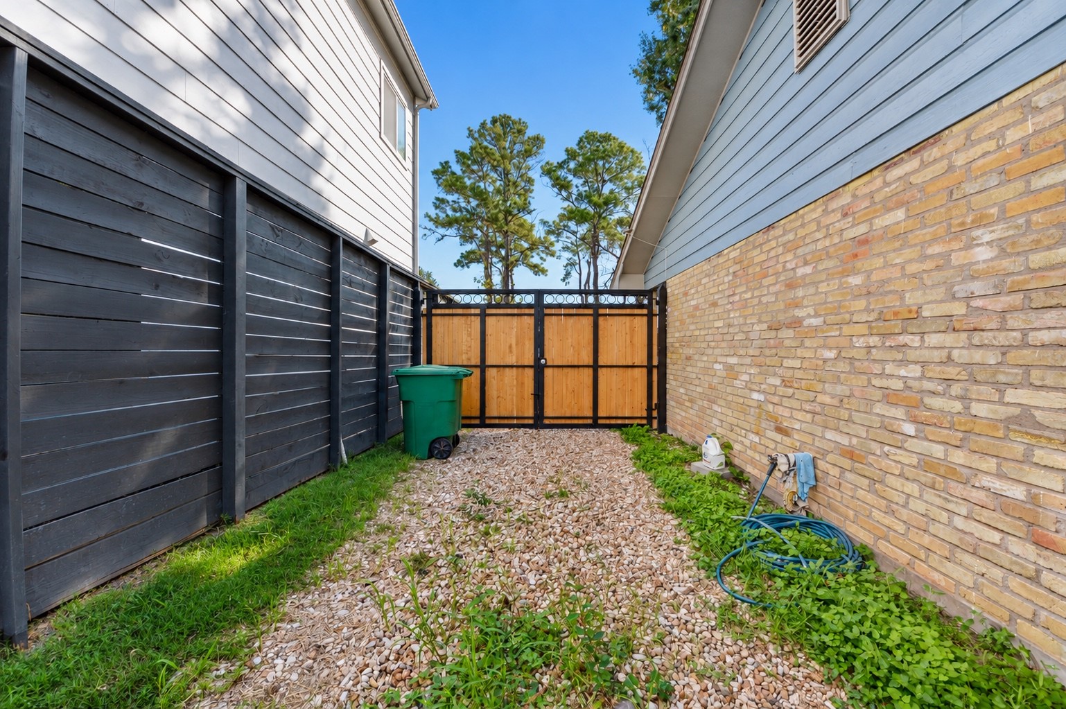 Charming side yard with a mix of gravel and grass, featuring a modern black fence and a wooden gate for added privacy.