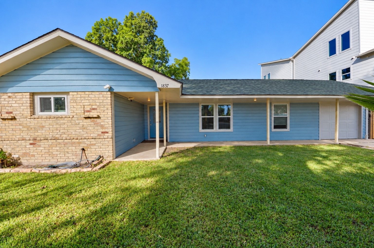 Charming single-story home featuring a mix of brick and blue siding, complemented by a lush, well-maintained front lawn and a covered entryway.