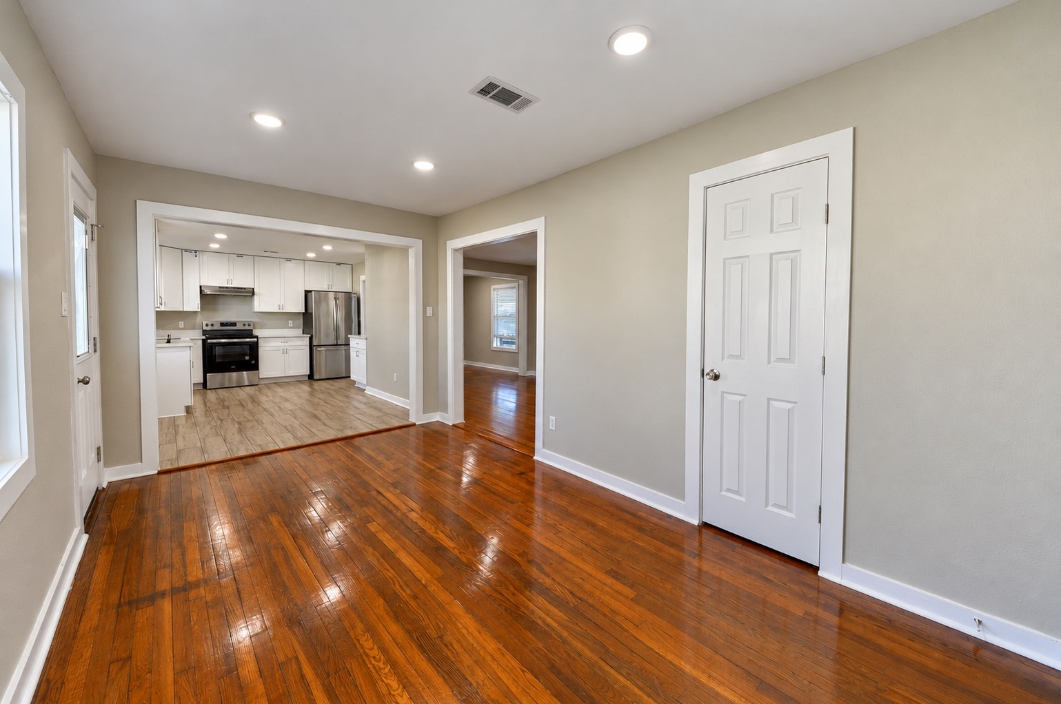 Charming living area with gleaming hardwood floors and recessed lighting, leading to a modern kitchen with stainless steel appliances and white cabinetry.