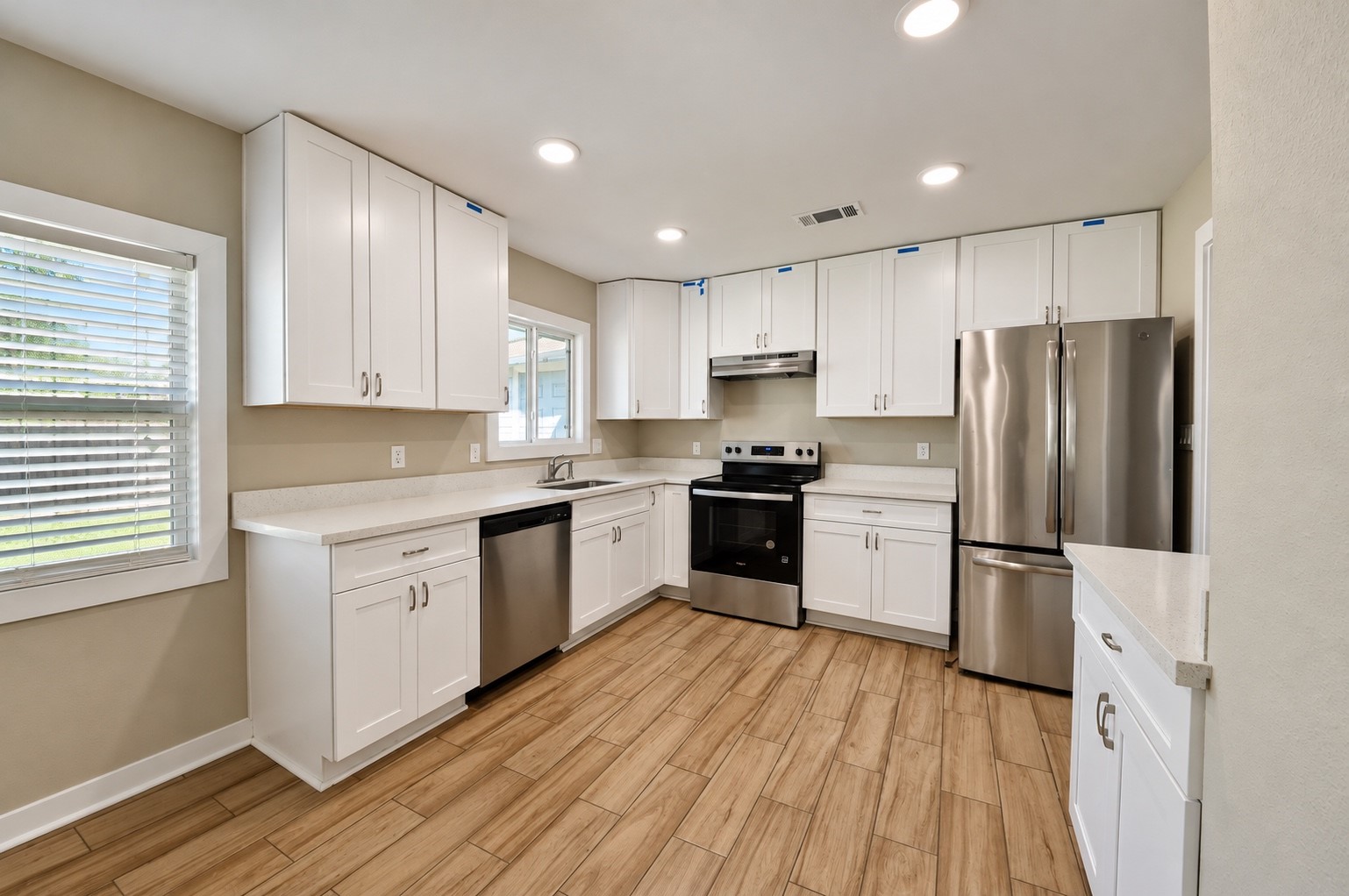 Bright and modern kitchen featuring sleek stainless steel appliances, crisp white cabinetry, and warm wood-look flooring, providing a perfect blend of style and functionality.