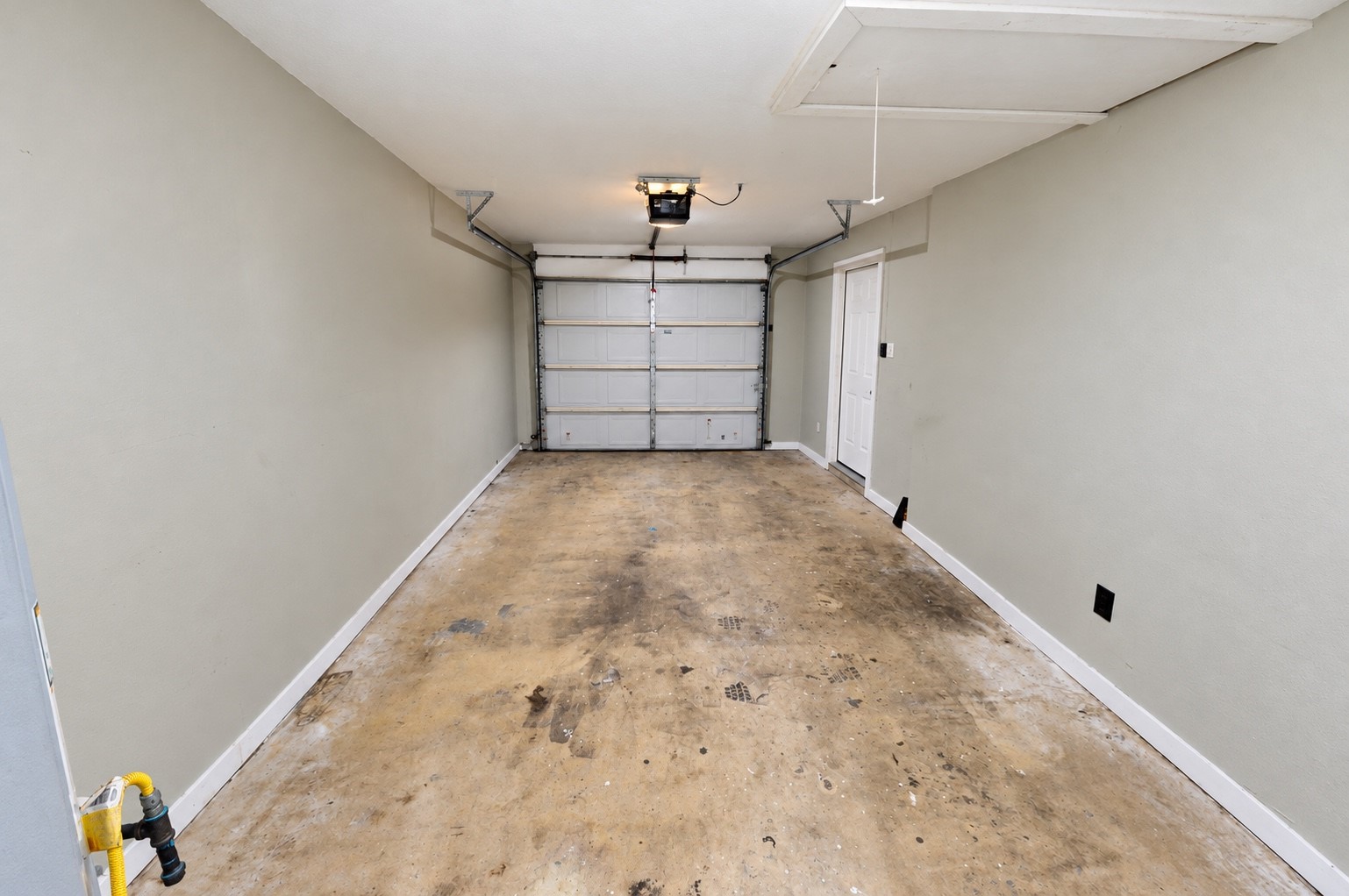 Spacious single-car garage with direct access door, featuring a durable concrete floor and automatic garage door opener for convenience.