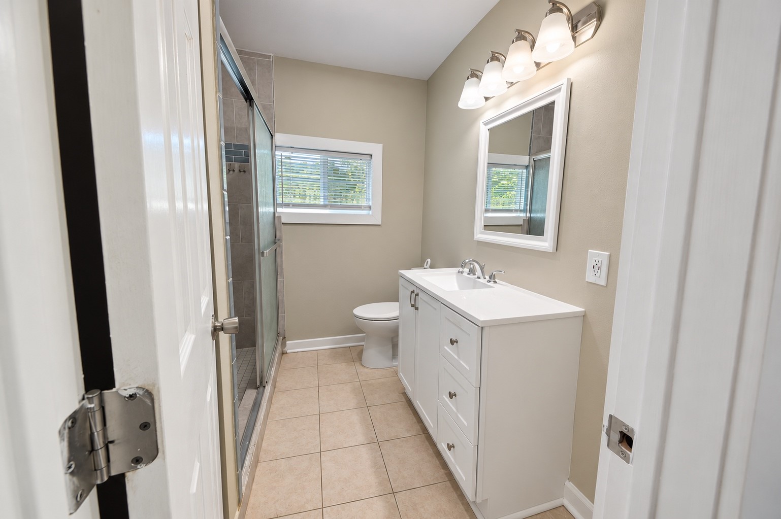 Modern bathroom featuring a sleek vanity with ample storage, a large mirror, and a glass-enclosed shower, complemented by stylish lighting and neutral tile flooring.