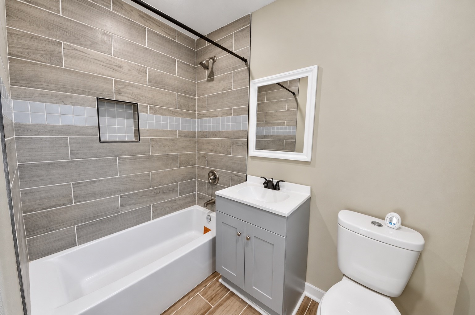 Charming bathroom with modern wood-look tile, a sleek vanity with a framed mirror, and a convenient shower-tub combination.