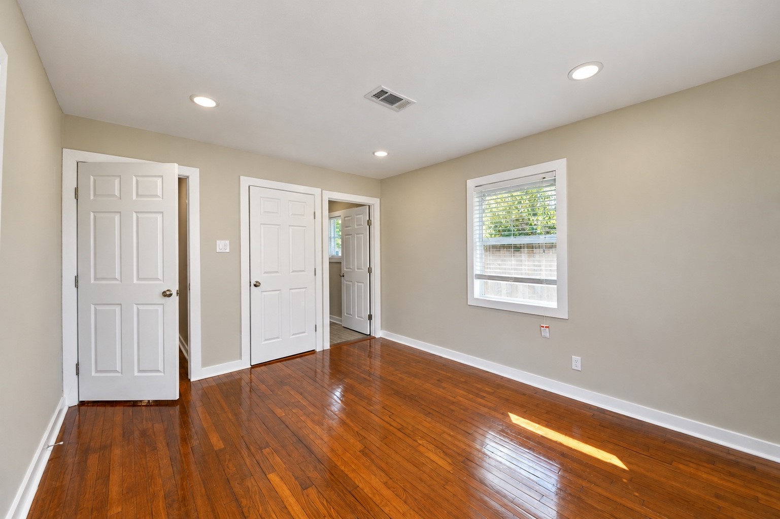 Bright, spacious room with gleaming hardwood floors, neutral walls, and ample closet space, perfect for versatile living.