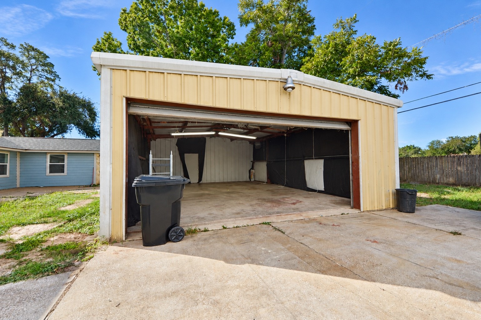 Spacious metal garage with ample room for storage or parking, set on a concrete driveway with surrounding greenery.