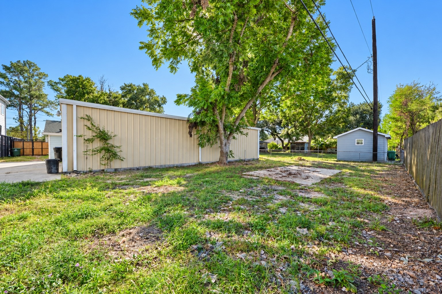 Spacious backyard featuring lush greenery, mature trees, and a concrete pad, perfect for outdoor activities and gardening or additional large vehicle parking.