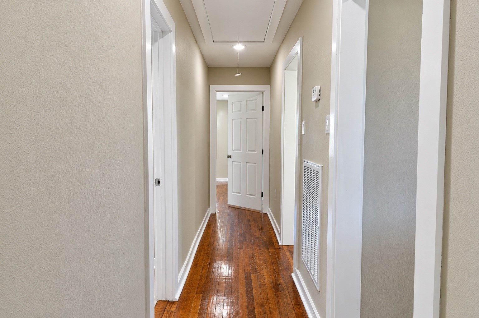 Bright and inviting hallway with polished hardwood floors and soft neutral walls, leading to a well-lit interior door.