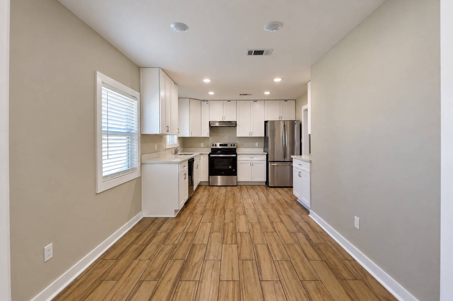 Sleek kitchen with modern stainless steel appliances, elegant white cabinetry, and warm wood-look tile flooring, offering a bright and inviting space for culinary creativity.