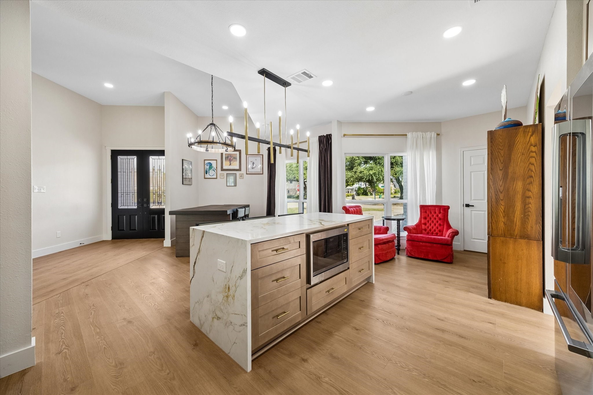 Modern open-concept space featuring a sleek kitchen island, elegant lighting, and seating area by a large window, offering a warm and inviting atmosphere.