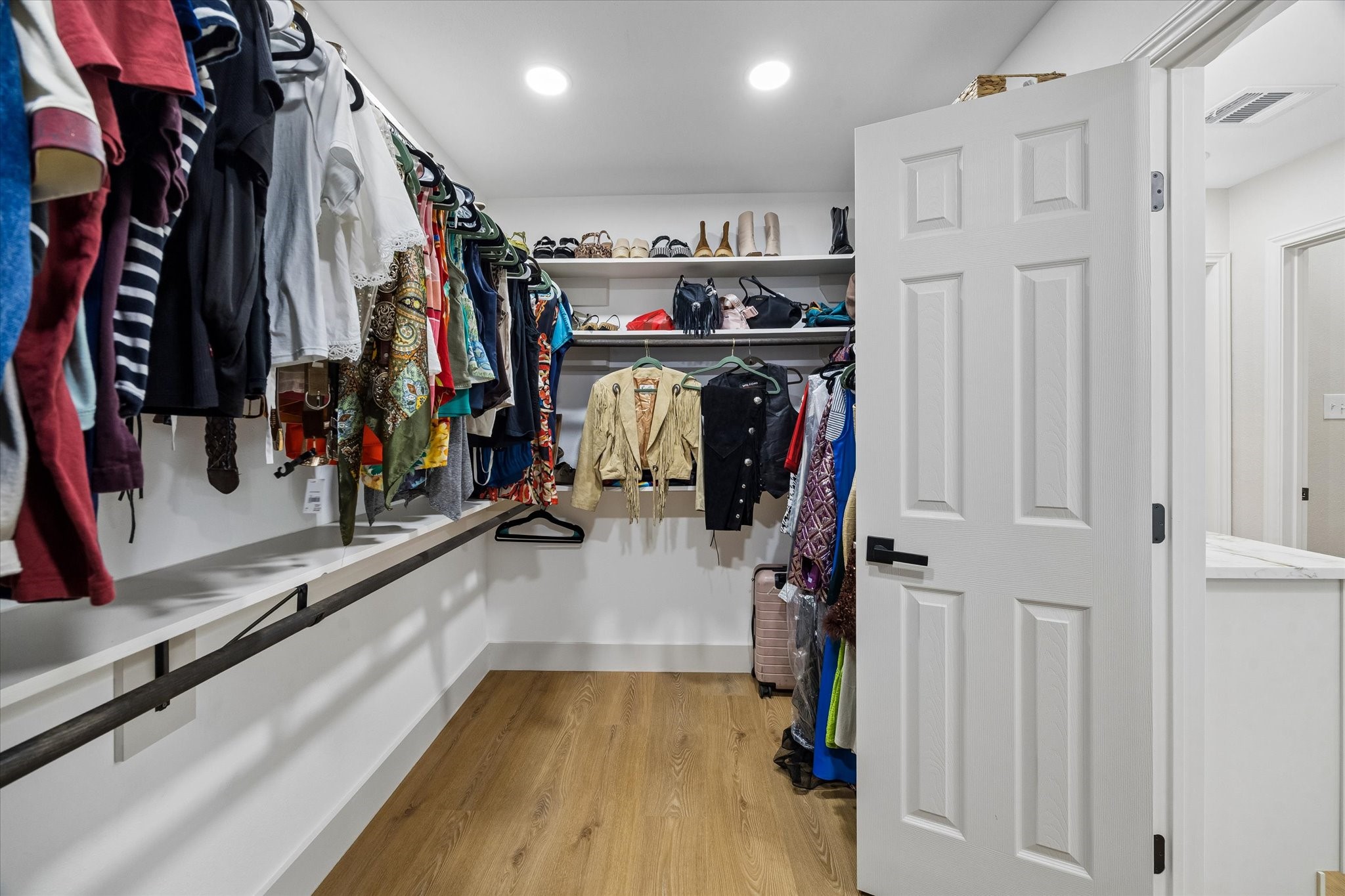 Spacious walk-in closet with ample hanging space, shelving for shoes and accessories, and elegant wood flooring.