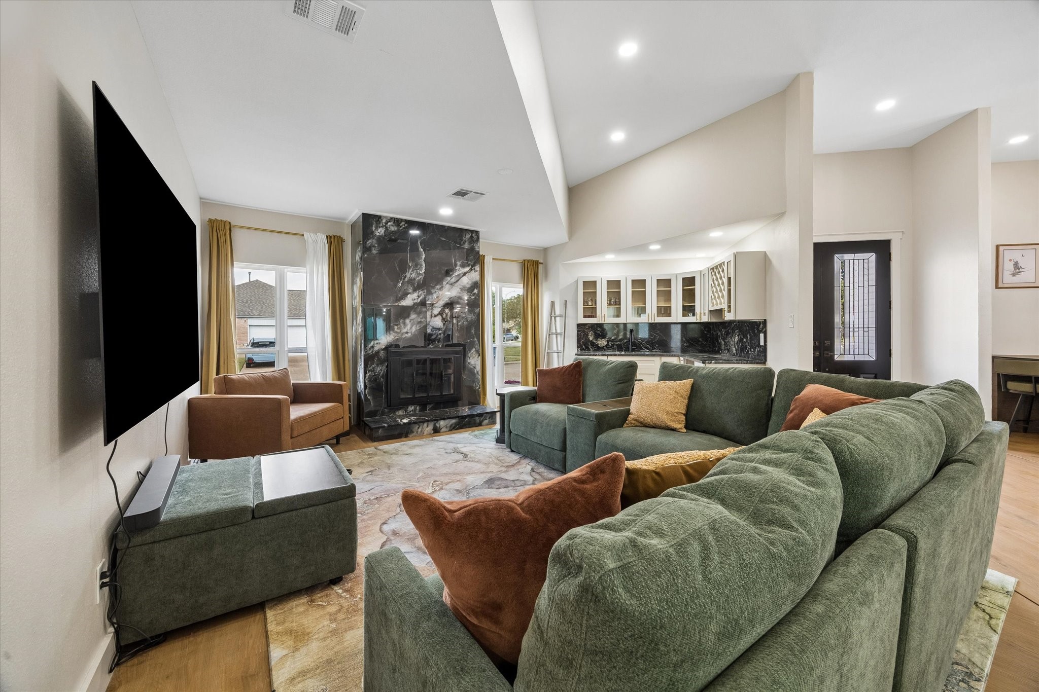 This spacious living room with a sleek black marble gas log fireplace, wet bar and abundant natural light from large windows is the heartbeat of this home.