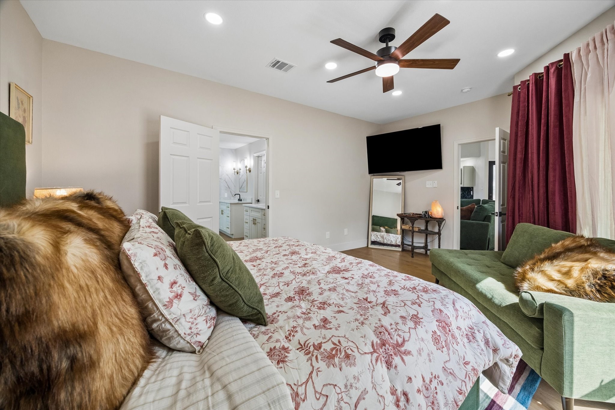 Another view of the primary bedroom with a stylish ceiling fan and floor to ceiling windows.  The room offers direct access to a chic bathroom with modern fixtures.