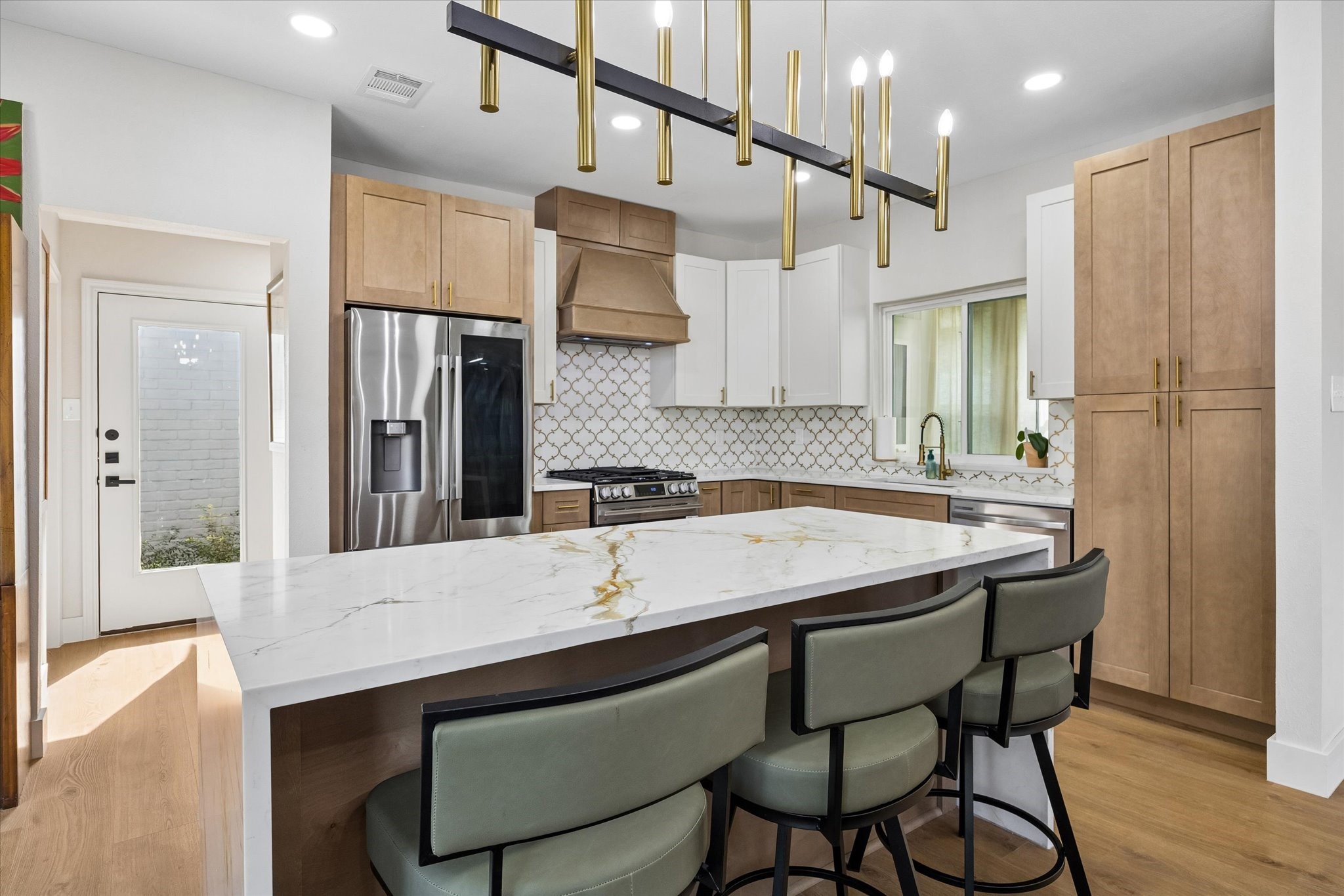 Sleek and modern kitchen featuring a large island with stainless steel appliances, and elegant light fixtures.